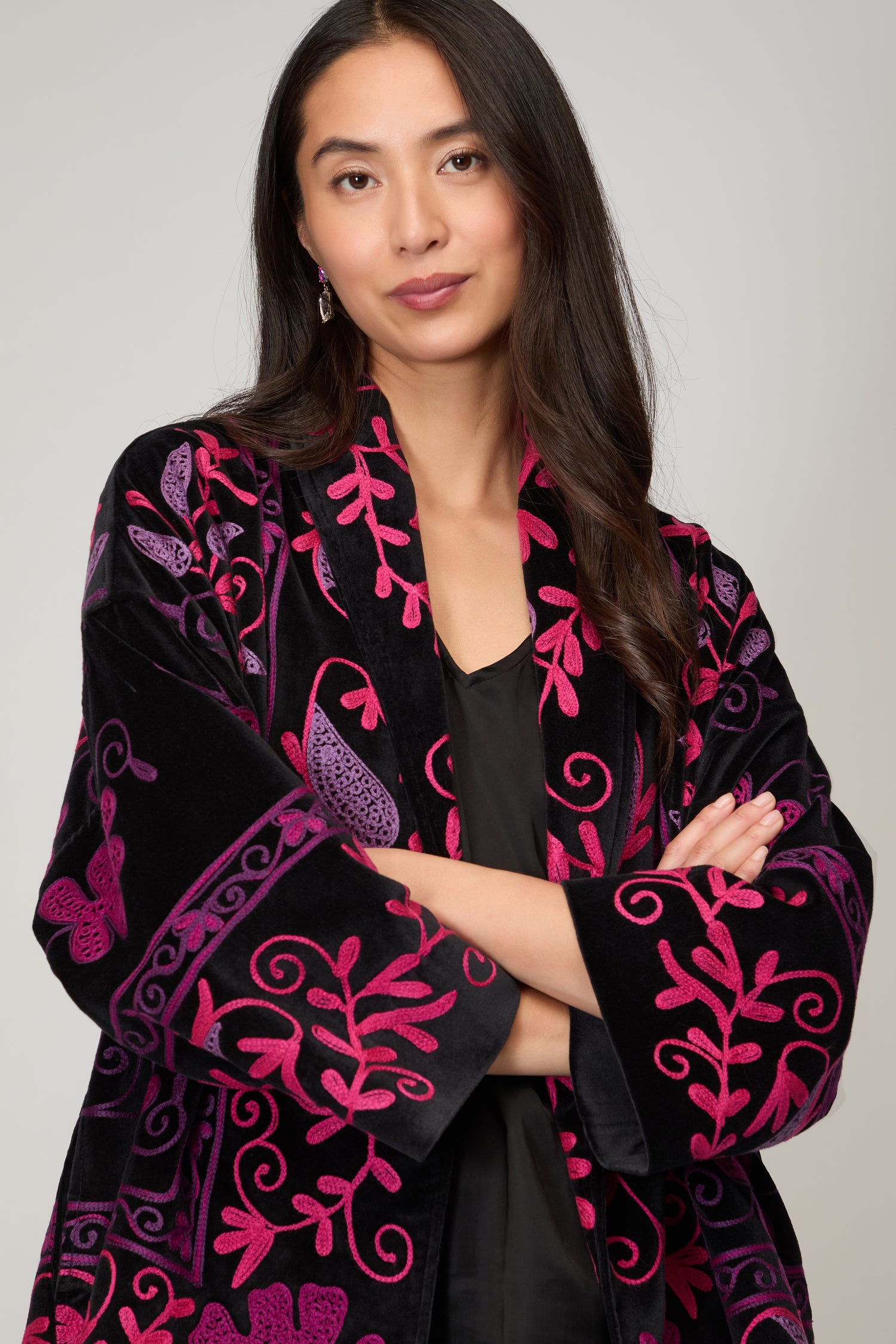Woman with long dark hair, arms crossed, wearing the Winter Embroidered Jacket featuring pink and purple floral patterns on black—an elegant choice for cooler days.