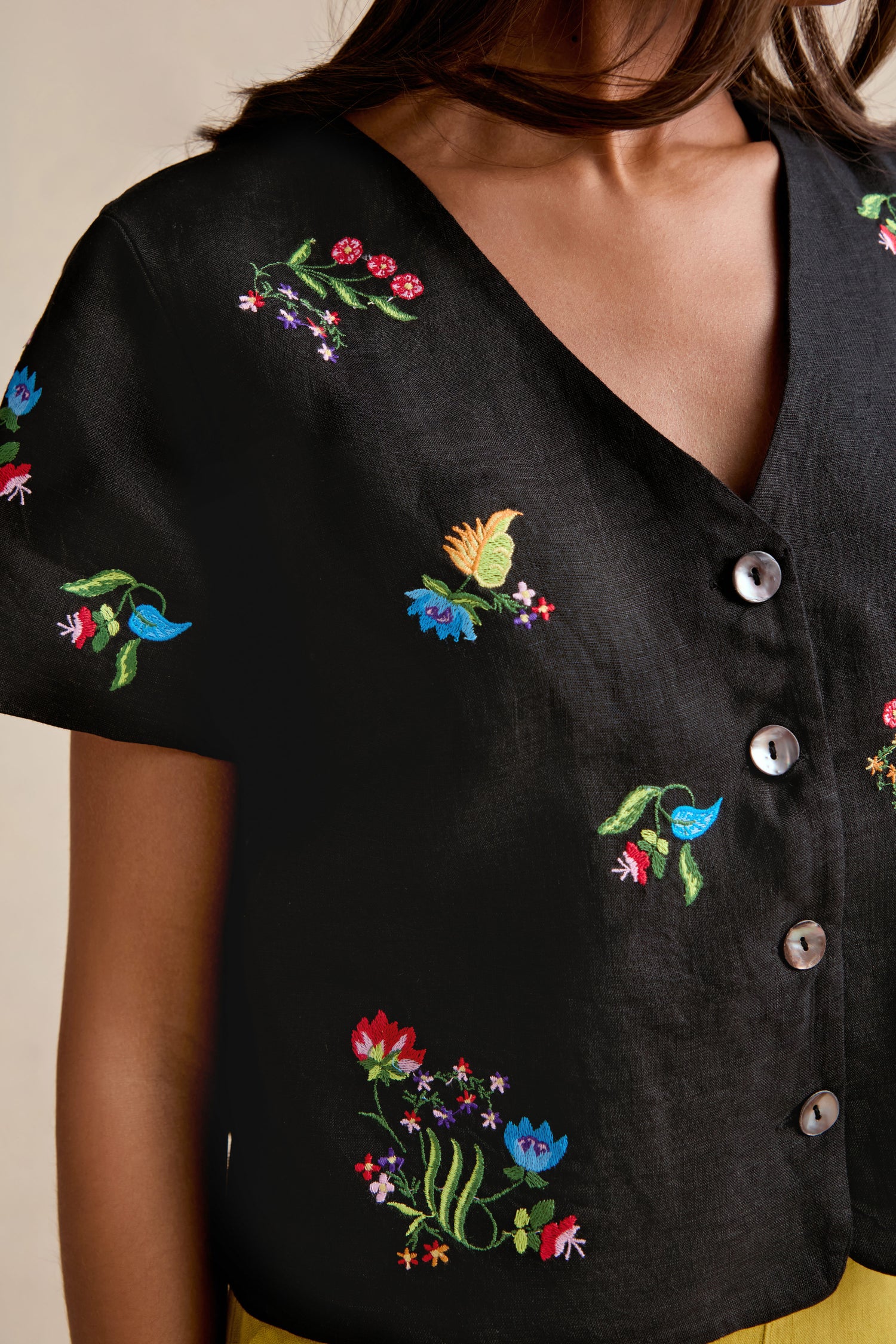 A woman wearing the Vintage Floral Embroidered Jacket, featuring black fabric, colorful floral embroidery, large round buttons, and a boxy silhouette.