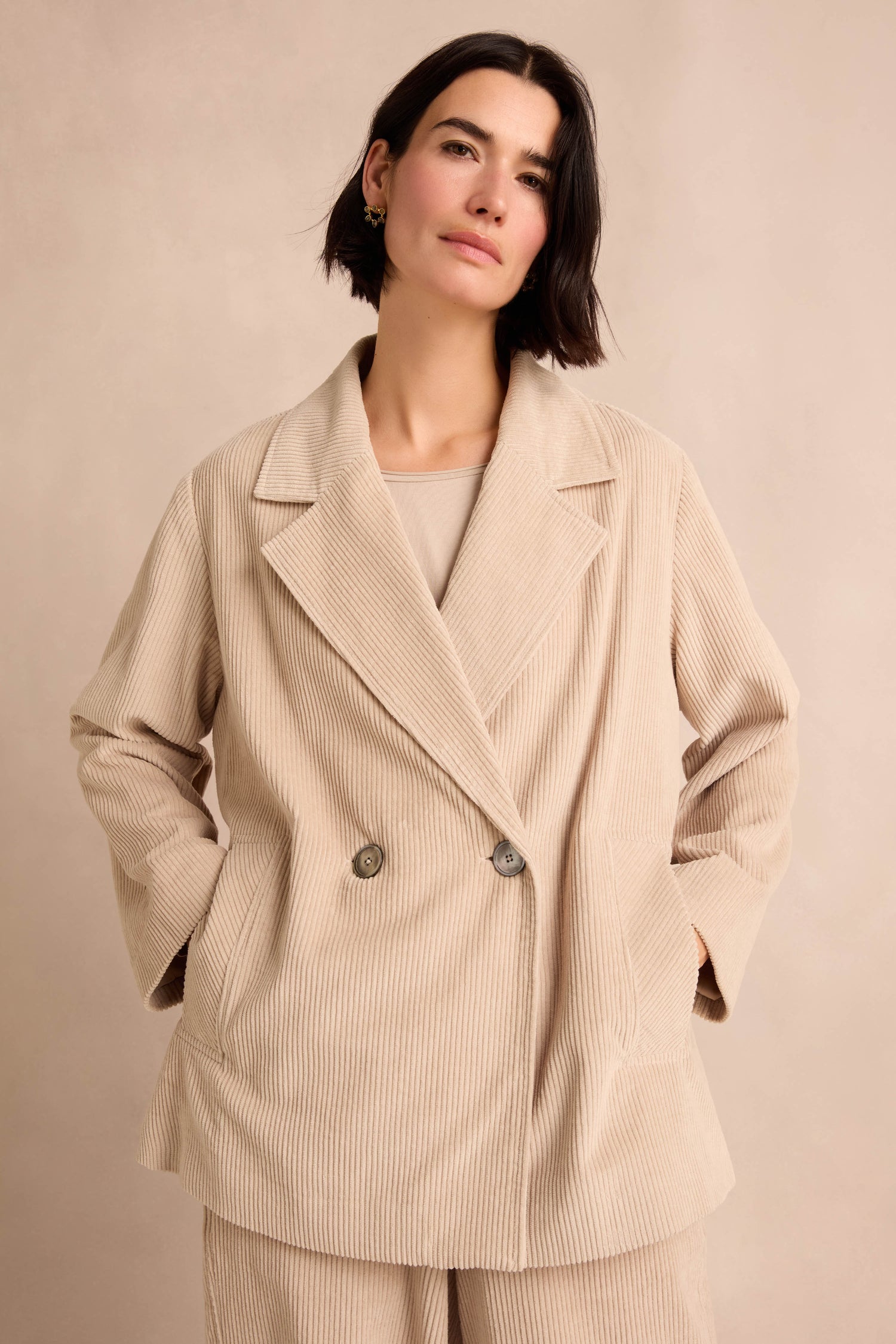Woman with short dark hair wearing the Ecru Jumbo Cord Caban Jacket and matching pants, standing against a neutral background with hands in pockets.