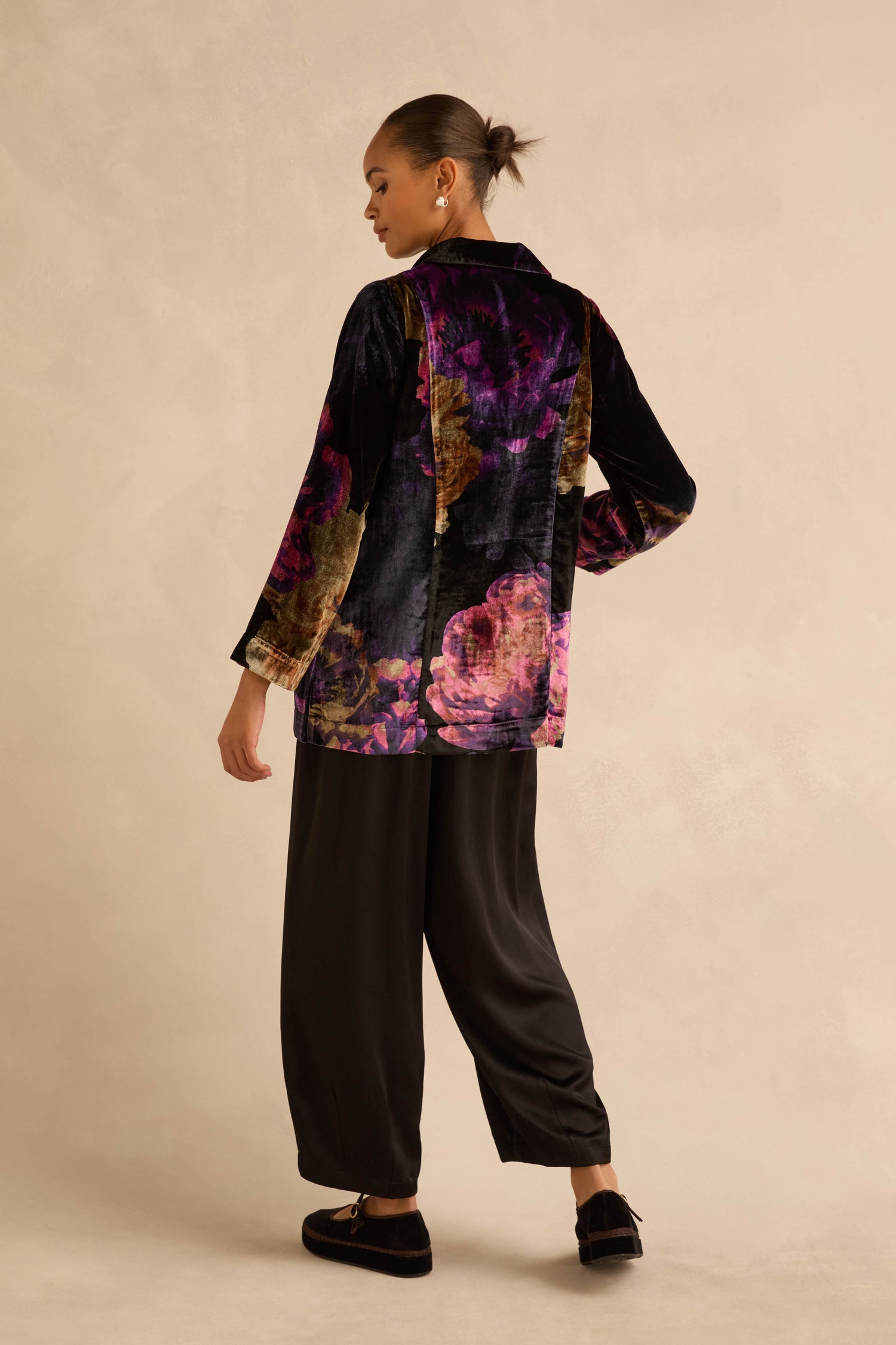 A person viewed from behind wearing a Midnight Peonies Velvet Relaxed Blazer, paired with wide-leg black trousers and black slip-on shoes.