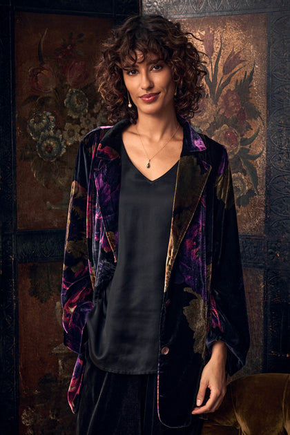 A person wearing a Midnight Peonies Velvet Relaxed Blazer in a relaxed-fit floral print over a black v-neck top.