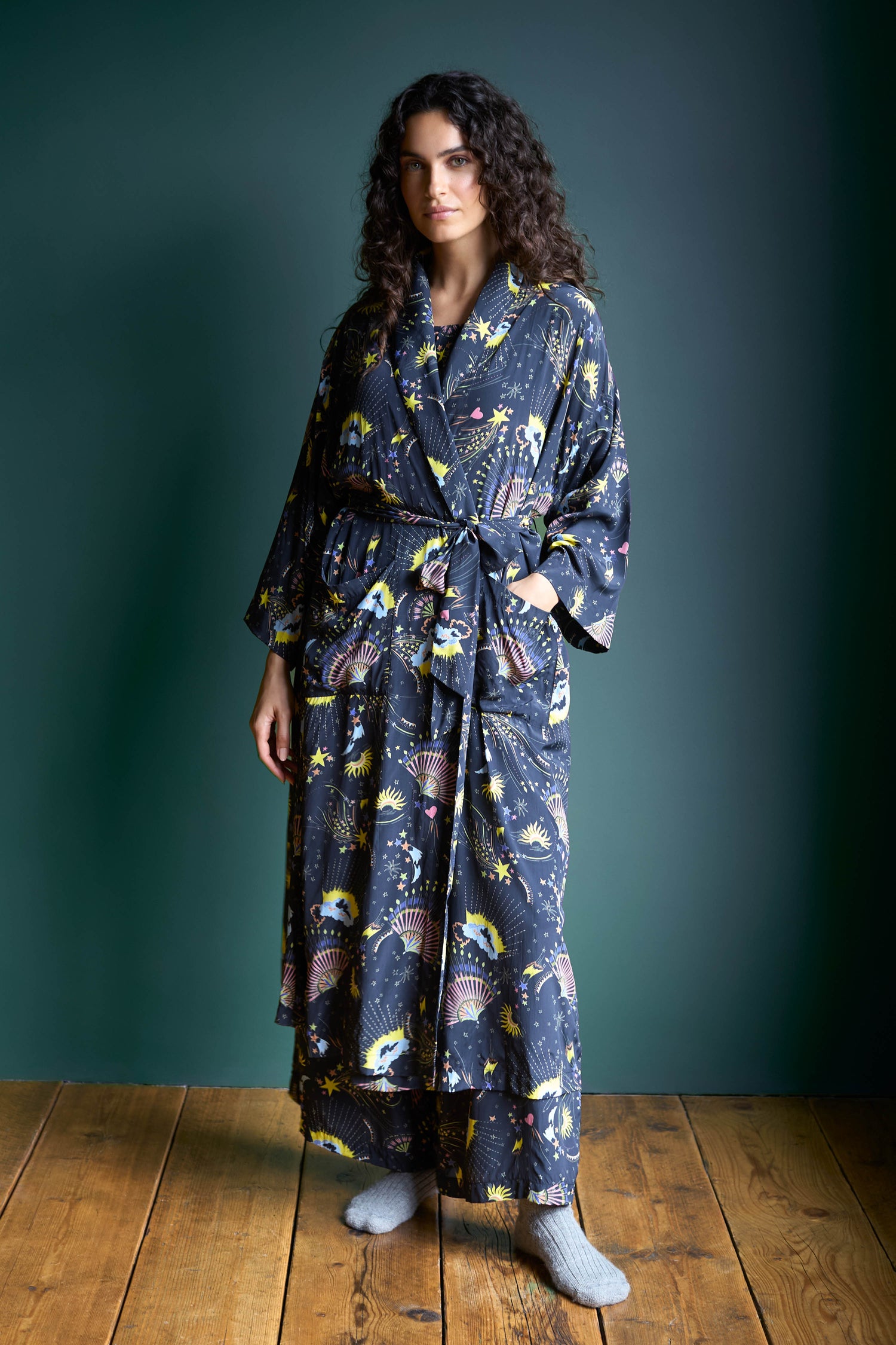 A person wearing a Celestial Dreams Robe and GRN6199-CD socks stands elegantly on a wooden floor, set against a dark green background.