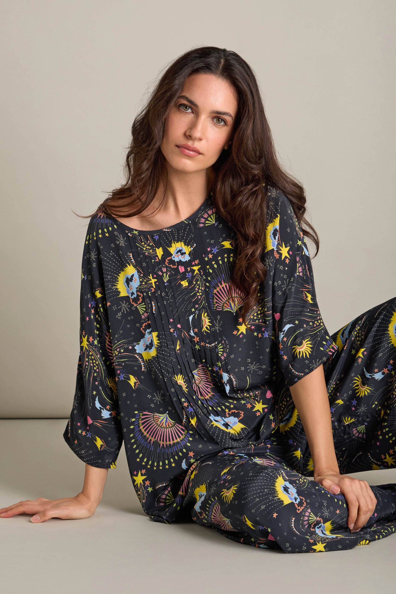 A woman sits gracefully, dressed in a celestial-themed set that mirrors the luxury of a night's sleep, as though crafted from the fabric of the Celestial Dreams Pyjama Set.