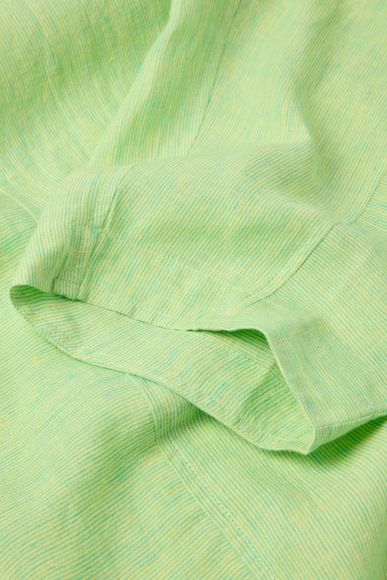 Close-up of the Linen Ticking Stripe Bubble Trouser in a light green and white classic ticking stripe pattern, highlighting the textured fabric and delicate pleats.