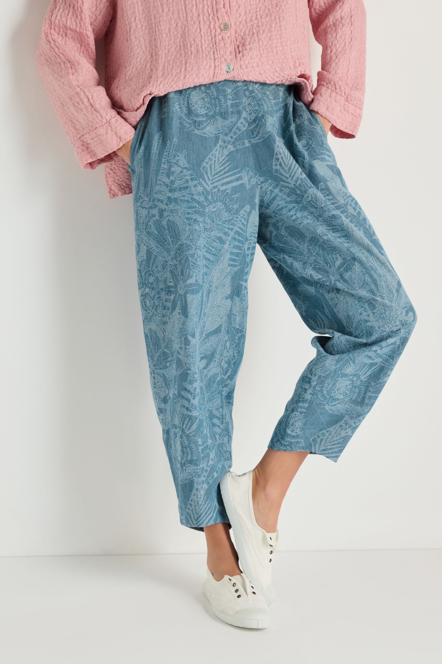 A person wearing a pink textured long-sleeve top, Floral Jacquard Cotton Bubble Trouser in denim blue, and white sneakers stands against a plain white background.