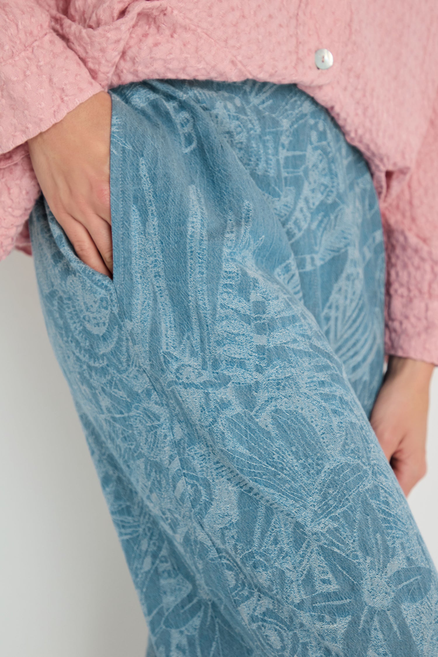 A person wears the Floral Jacquard Cotton Bubble Trouser in blue with a pink textured shirt, one hand in their pocket.