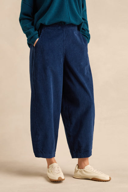 Wearing the Marine Jumbo Cord Bubble Trousers in a relaxed bubble silhouette, styled with a teal sweater and white sneakers, the person stands with hands in pockets against a neutral background.