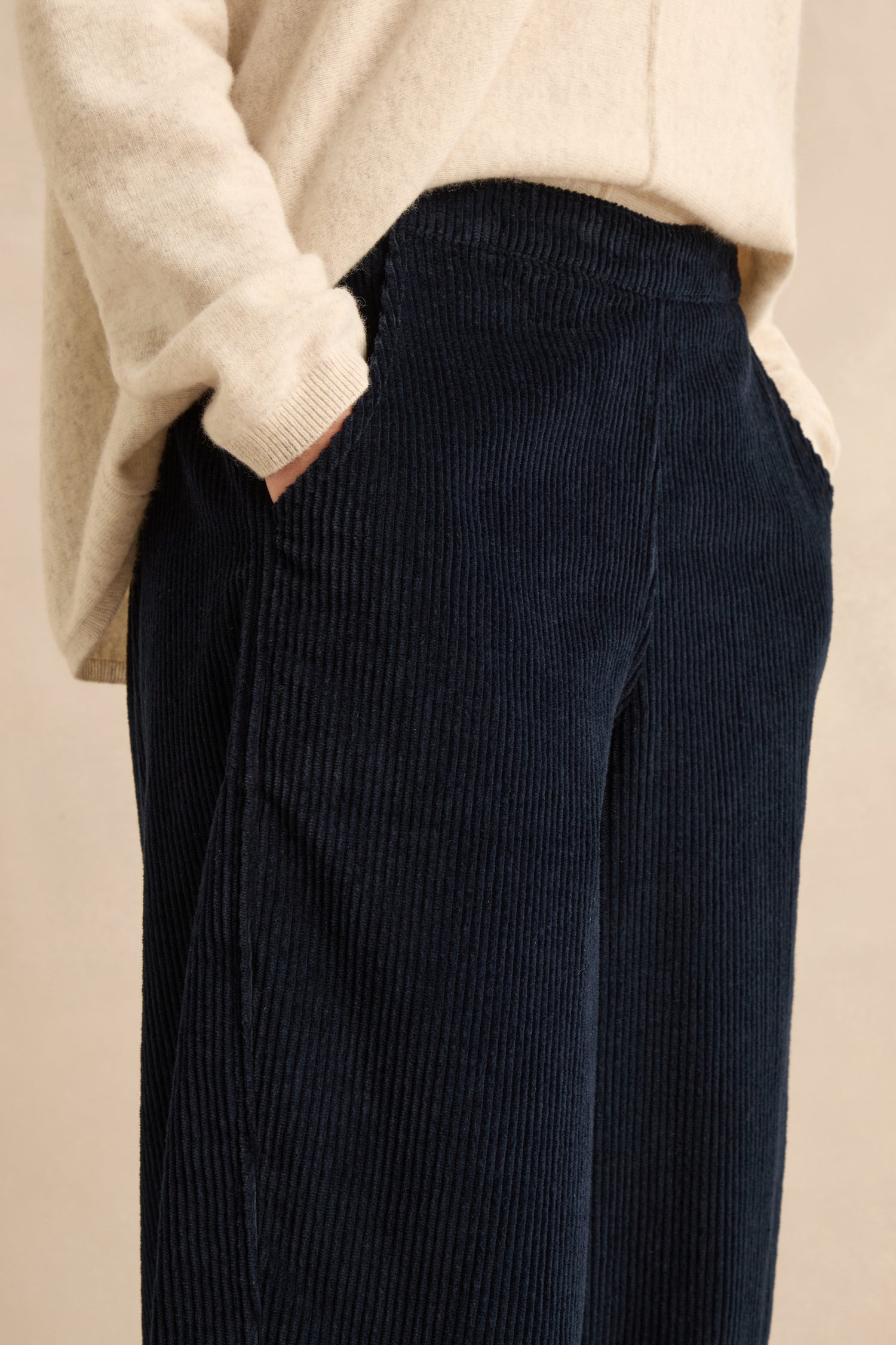 A person wearing a cream sweater with their hands in the pockets of Navy Jumbo Cord Bubble Trousers, crafted from pure cotton and featuring a relaxed bubble silhouette.