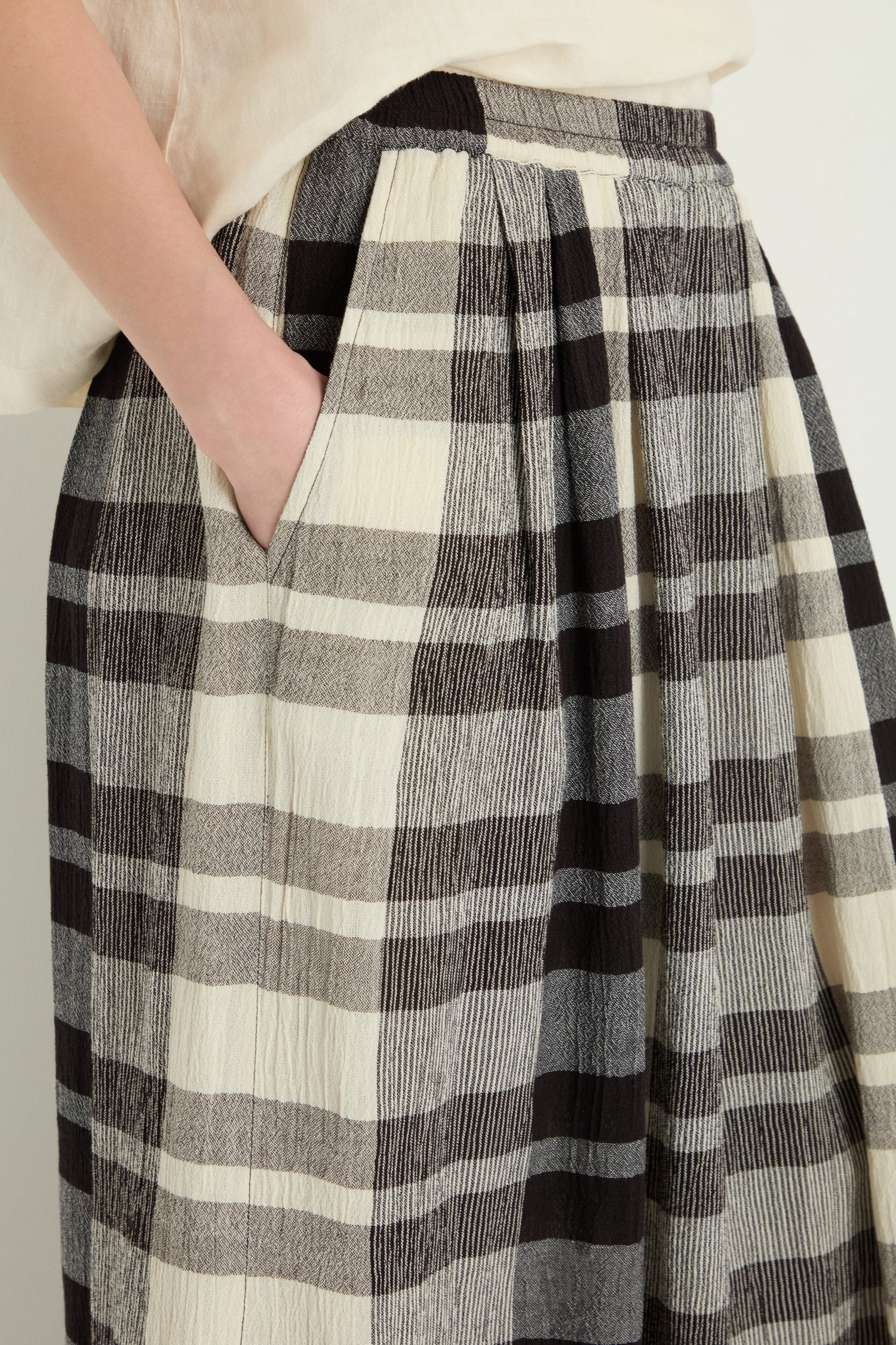 A person wearing a cream top and Monochrome Crinkle Check Wide Trousers with one hand placed in the trouser pocket.