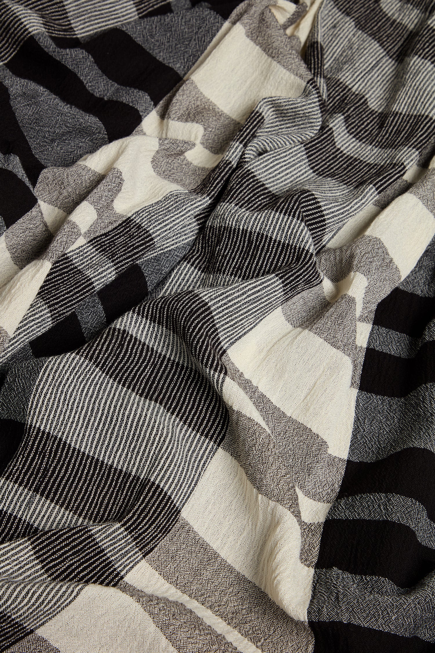 A close-up of crinkled fabric in a black, beige, and gray geometric check pattern, highlighting subtle folds—ideal for creating the Monochrome Crinkle Check Wide Trouser.