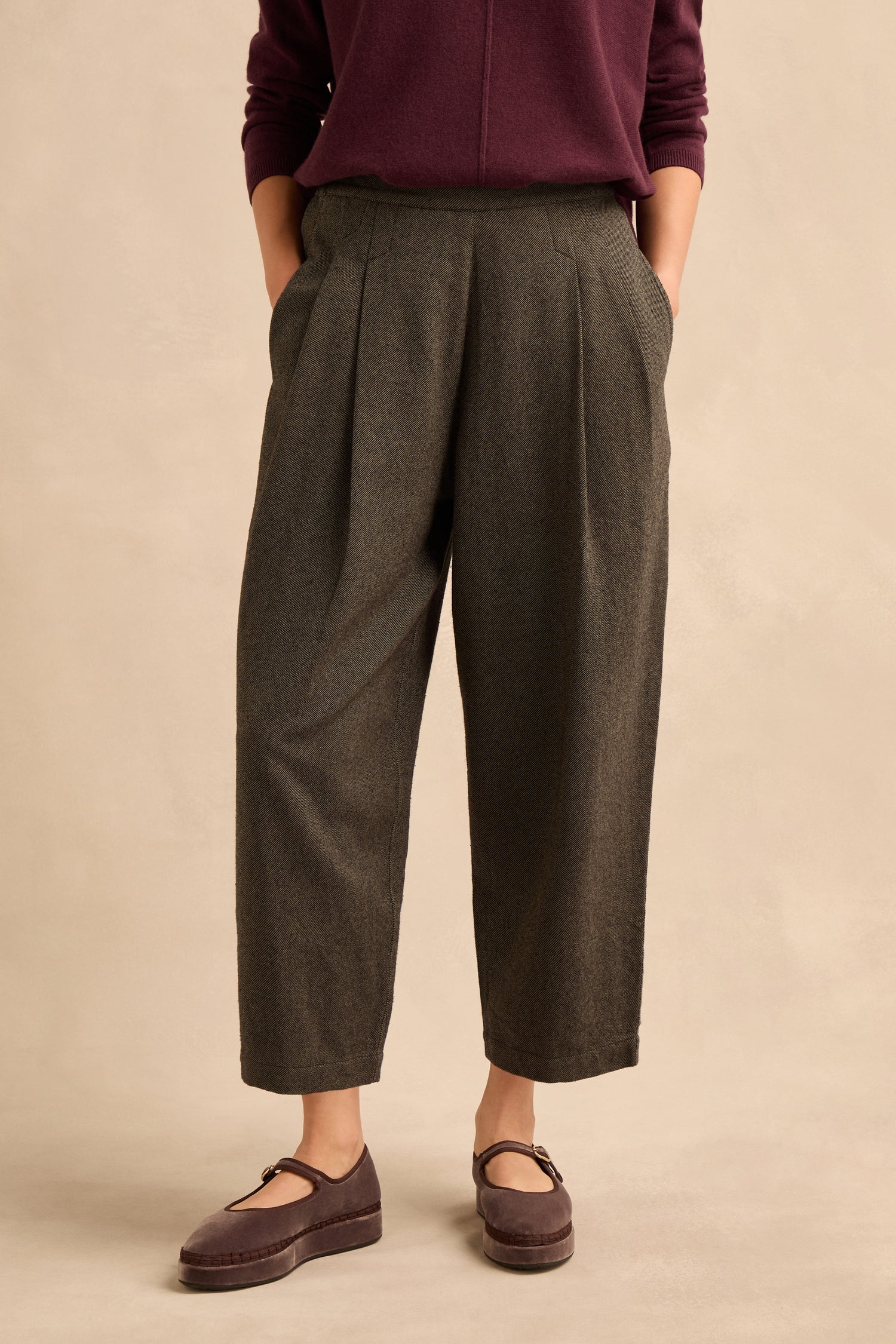 A person wearing a burgundy long-sleeve top, the Overdyed Twill Barrel Trouser in gray, and maroon Mary Jane shoes stands against a neutral background with hands in their pockets.