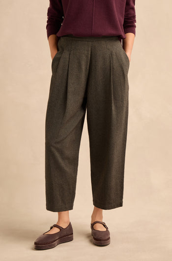 A person wearing a burgundy long-sleeve top, the Overdyed Twill Barrel Trouser in gray, and maroon Mary Jane shoes stands against a neutral background with hands in their pockets.