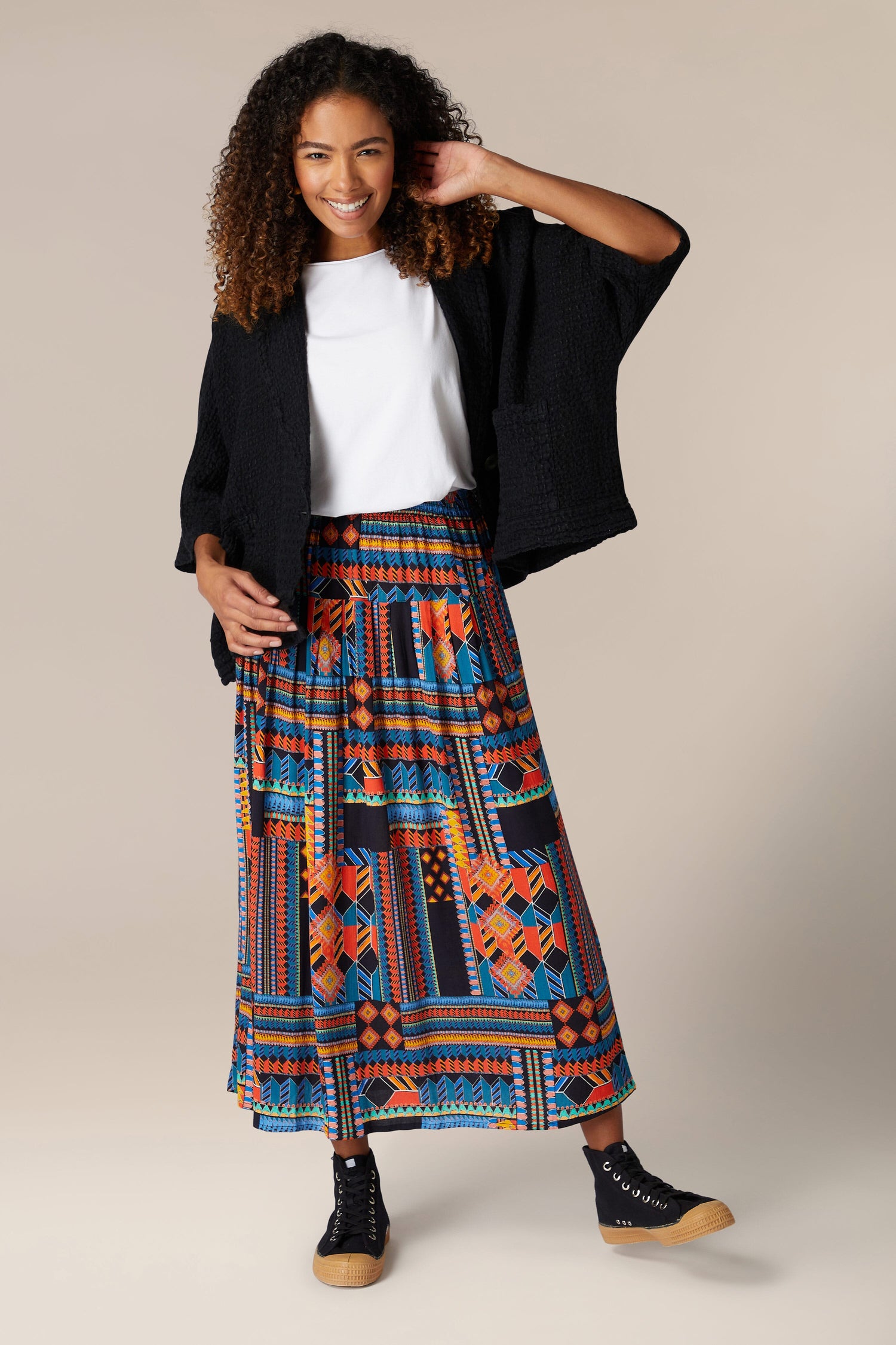 A woman wearing a flowing, vibrant Bold Graphic Printed Skirt and a black jacket.