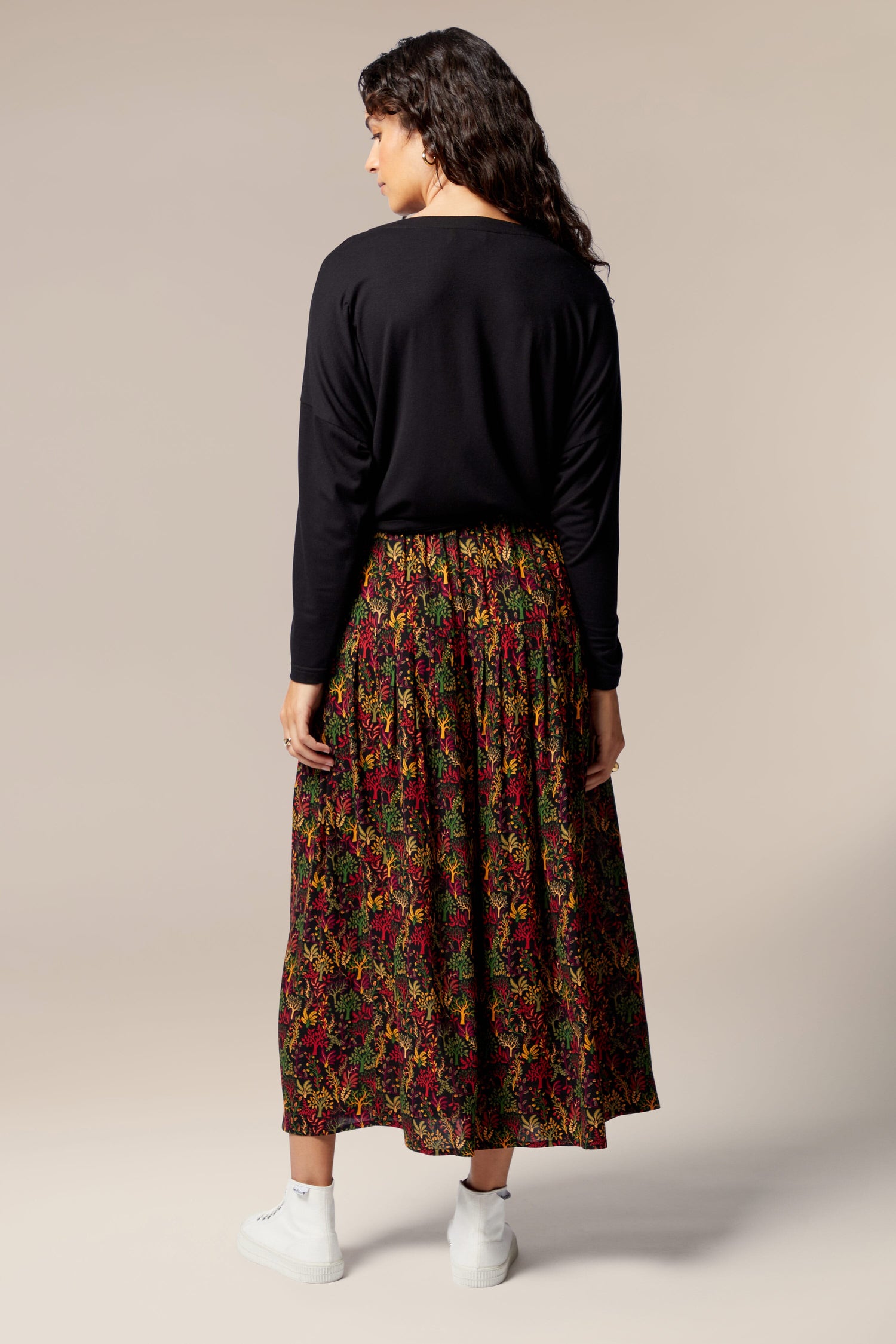 The back view of a woman wearing a black top and Magical Forest print skirt with autumnal tones.