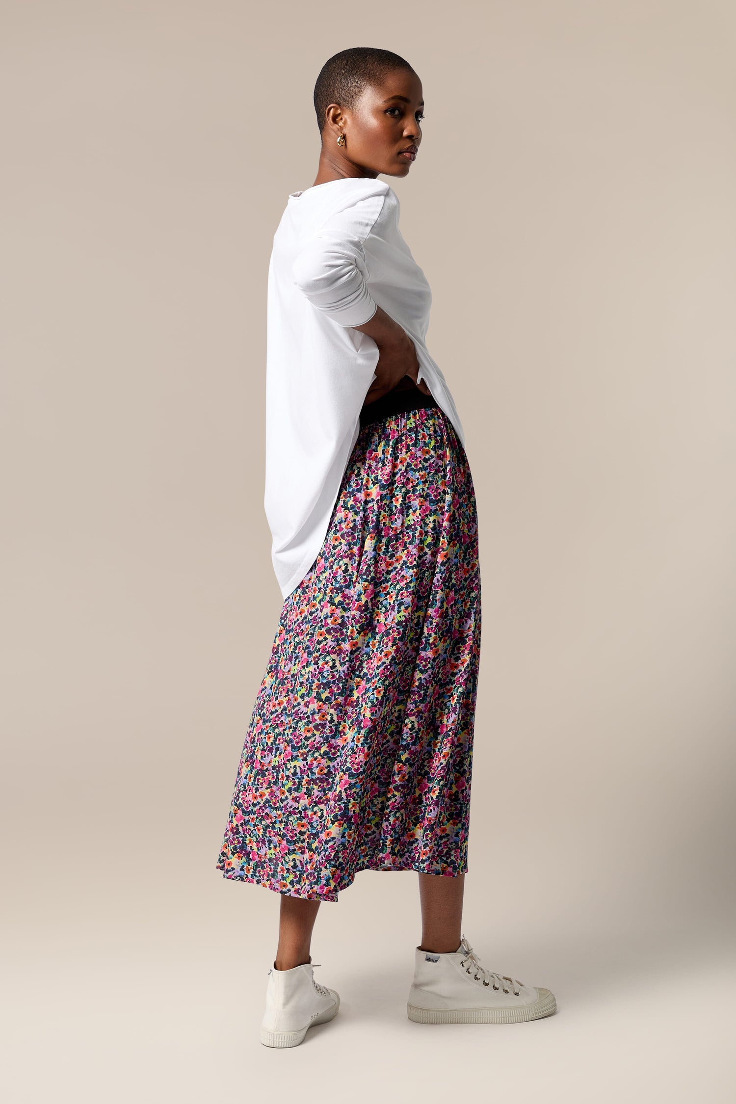 A woman wearing a swing silhouette in a Miniature Floral Garden Skirt made from planet-friendly viscose material, paired with a simple white t-shirt.