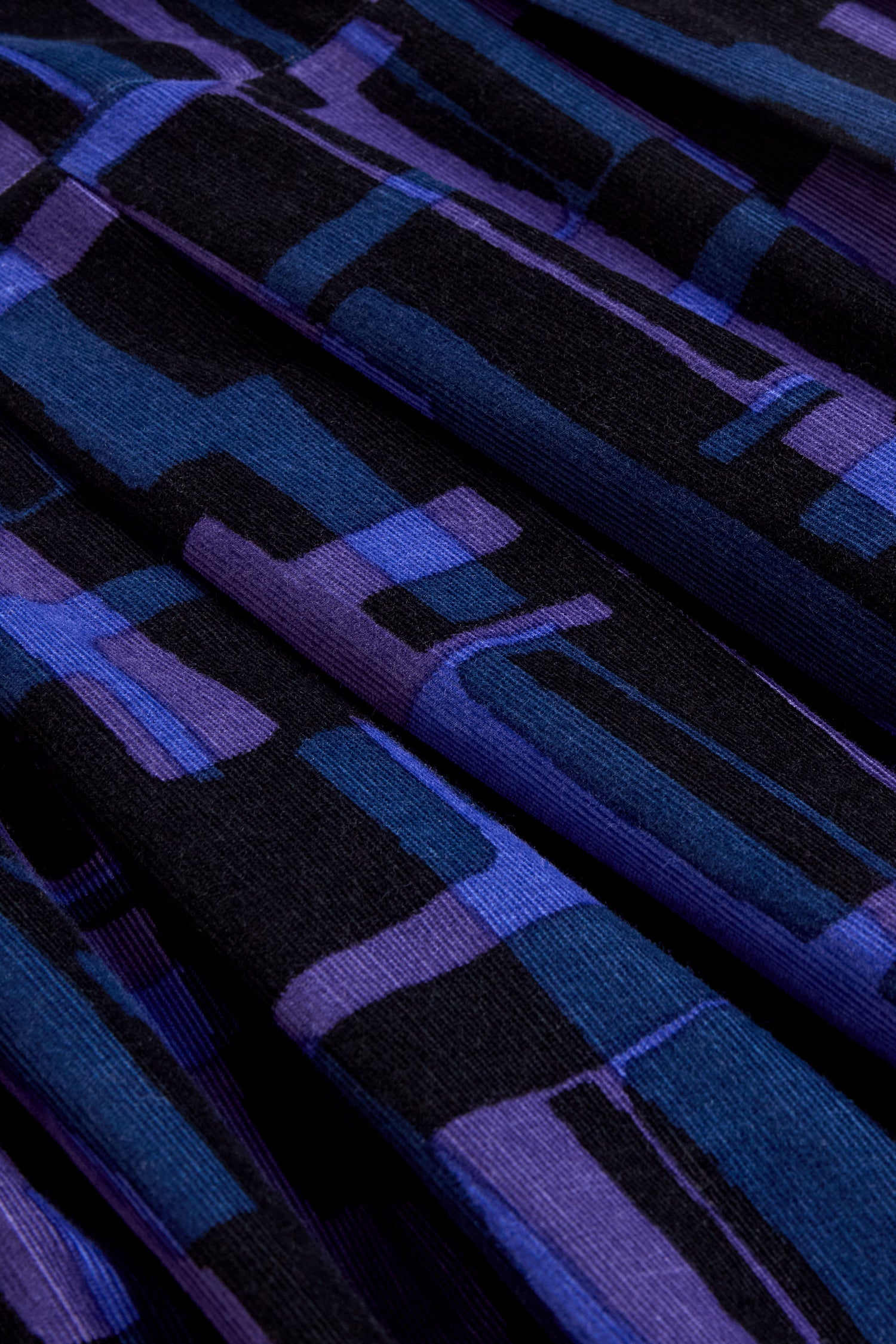 Close-up of folded fabric from the Layered Geometric Cord Skirt, showcasing a striking geometric pattern in shades of black, purple, and blue.