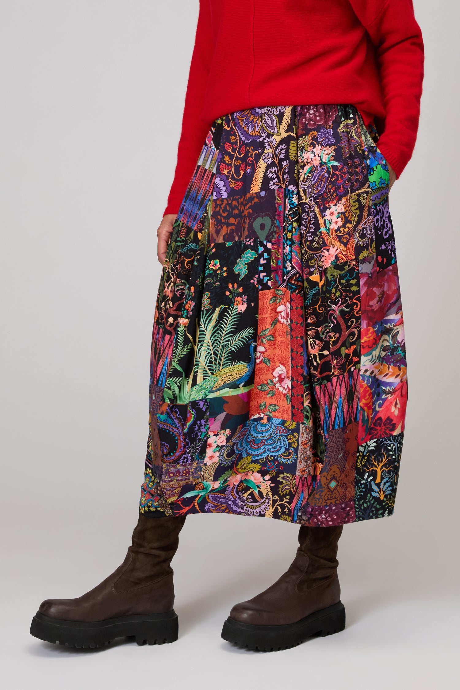 Person wearing a red top, Sahara Winter Patchwork Skirt, and dark brown boots, standing against a plain background.