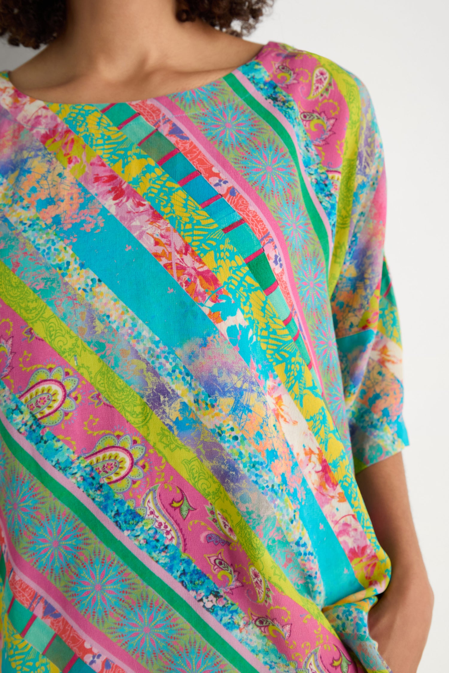 A person wearing the Patchwork Stripe Boxy Top featuring diagonal stripes with paisley and floral designs in pink, green, yellow, and turquoise archive prints for a vibrant look.