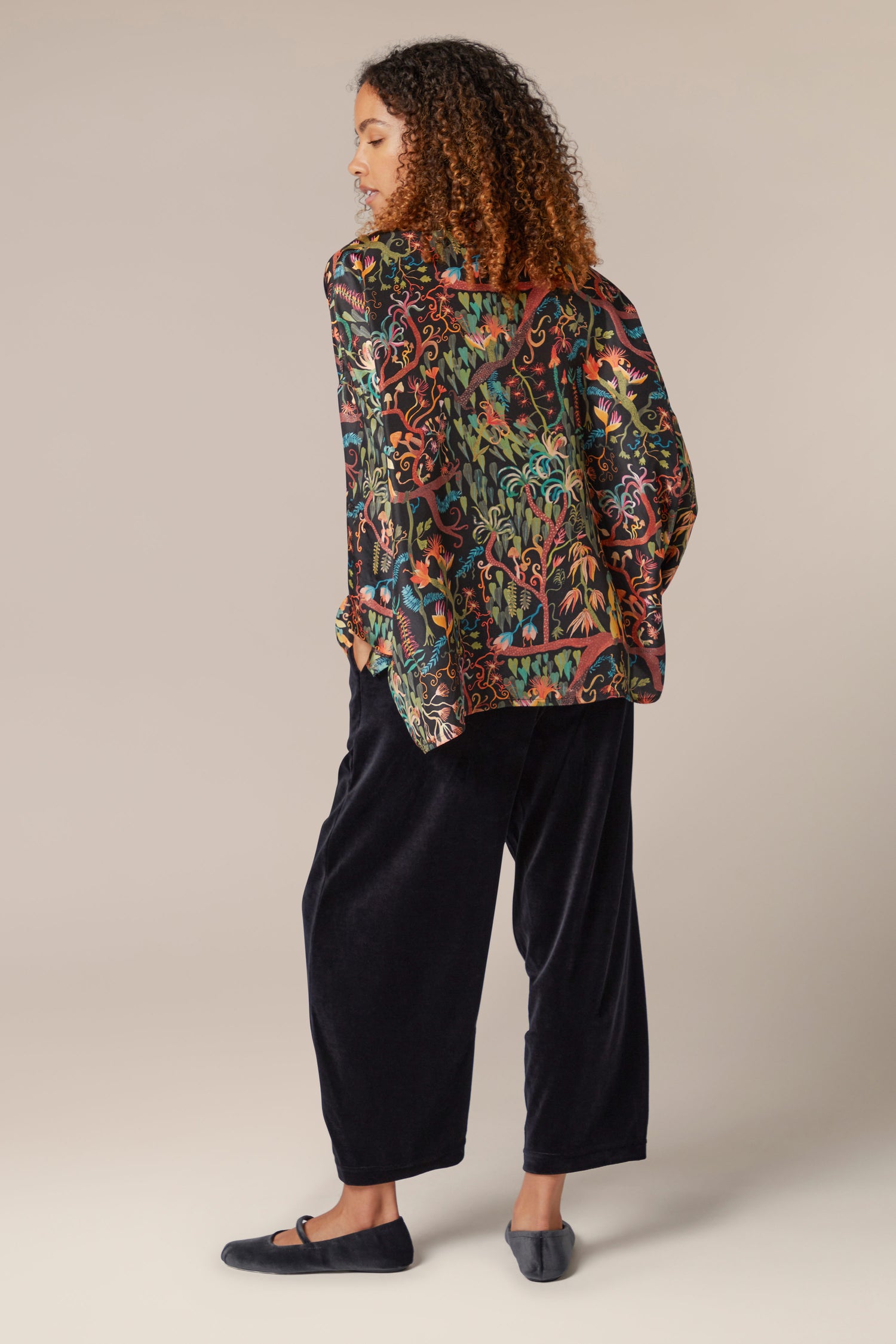 The back view of a woman wearing a Faraway Jungle Silk Boxy Shirt and black trousers.