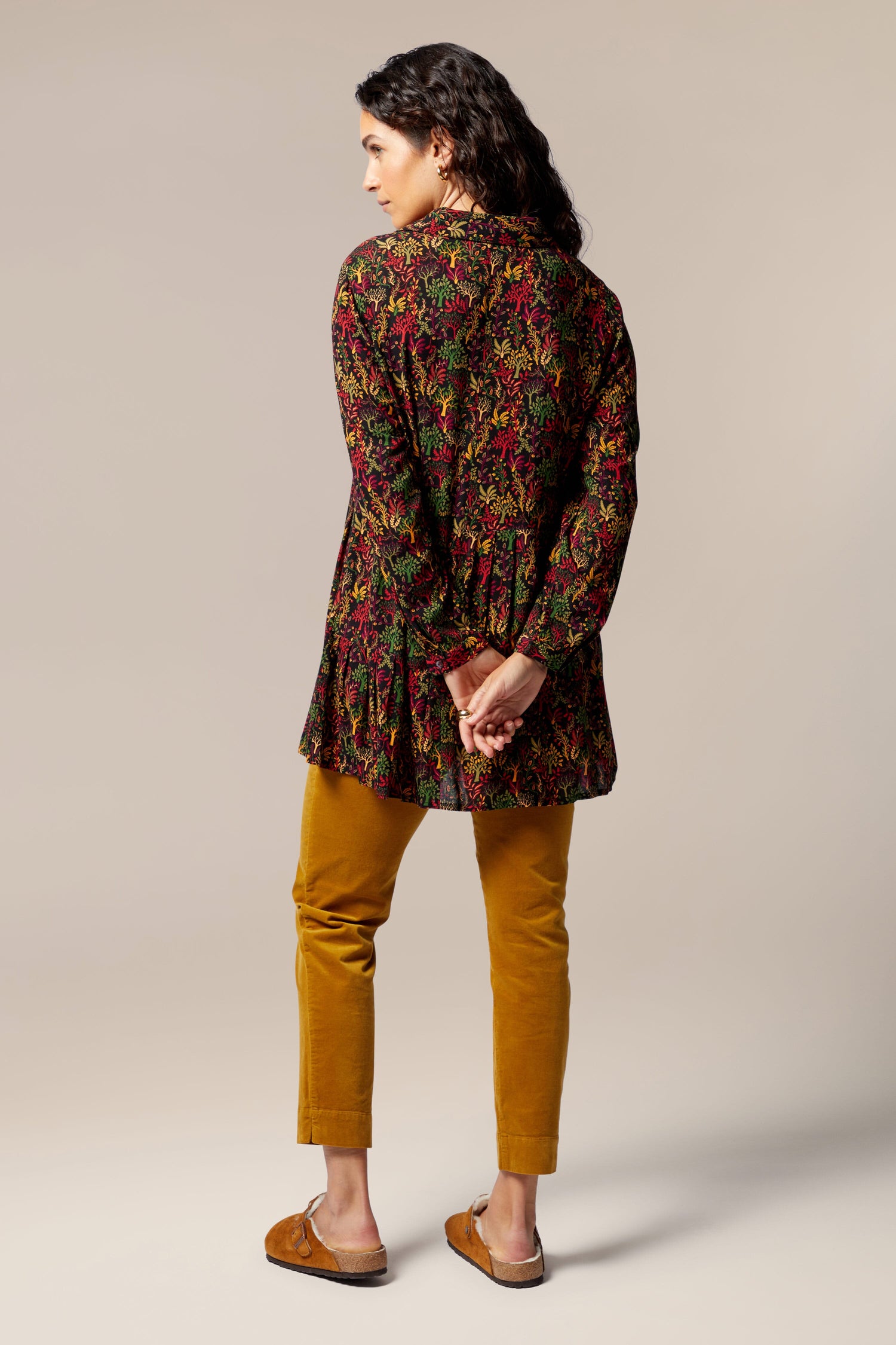 The woman's back view showcases her stunning swing silhouette with a floral tunic, pairing perfectly with autumnal tones and a touch of the magical forest print shirt on her yellow pants.