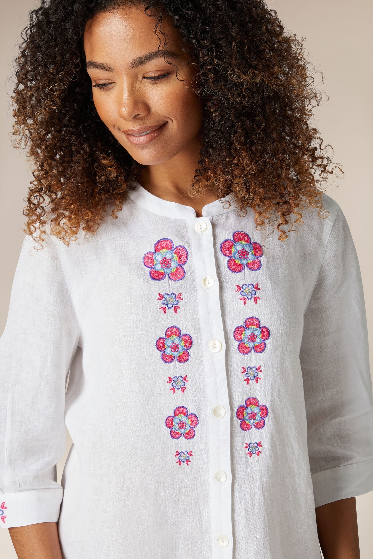 A woman with curly hair smiles gently, wearing a white pure linen Floral Embroidery Shirt.