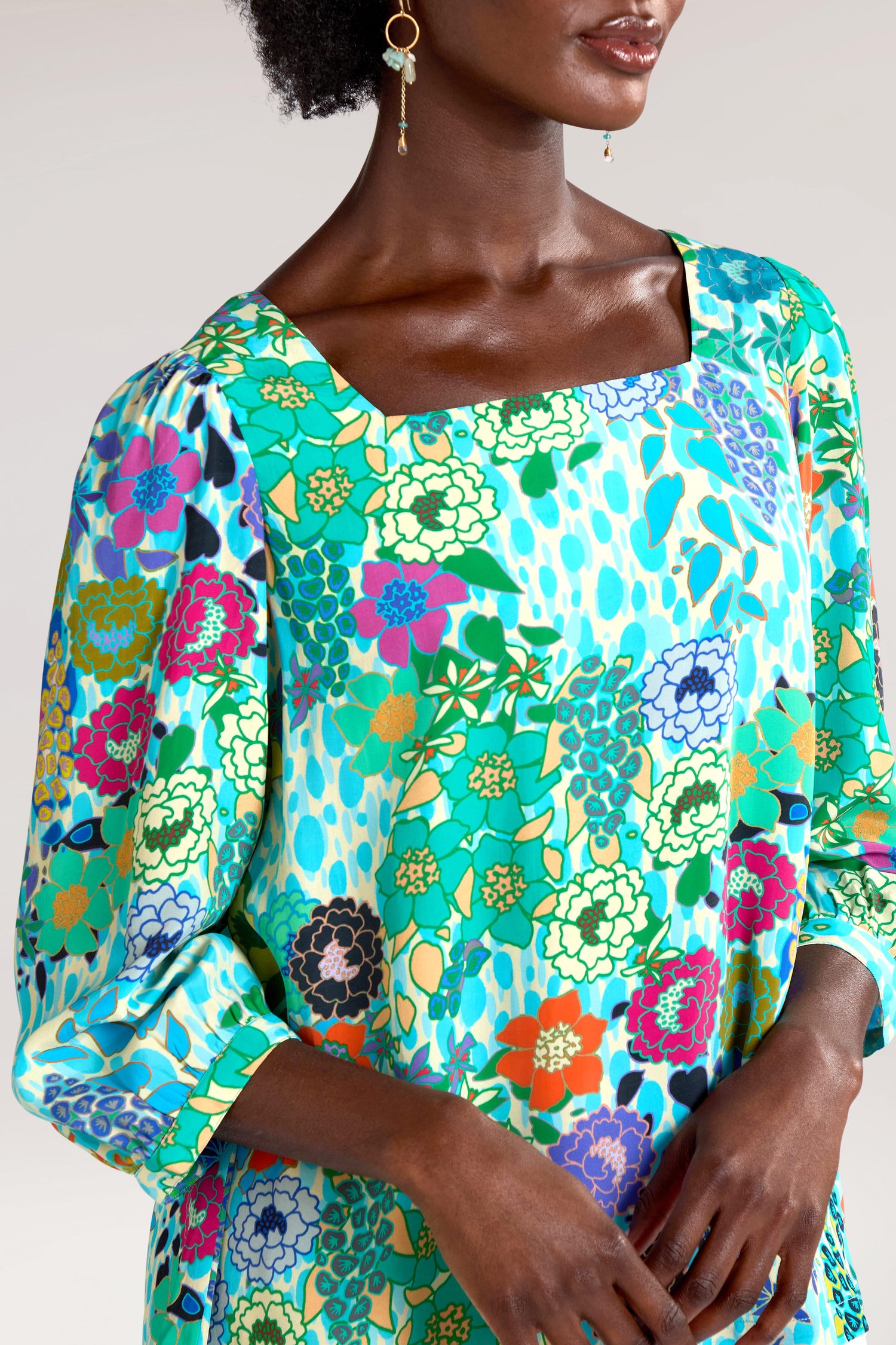 A person is wearing a colorful floral-patterned Garden Spot Square Neck Top with long sleeves. Made from draping viscose fabric, the attire flows beautifully against the plain background, evoking charm.