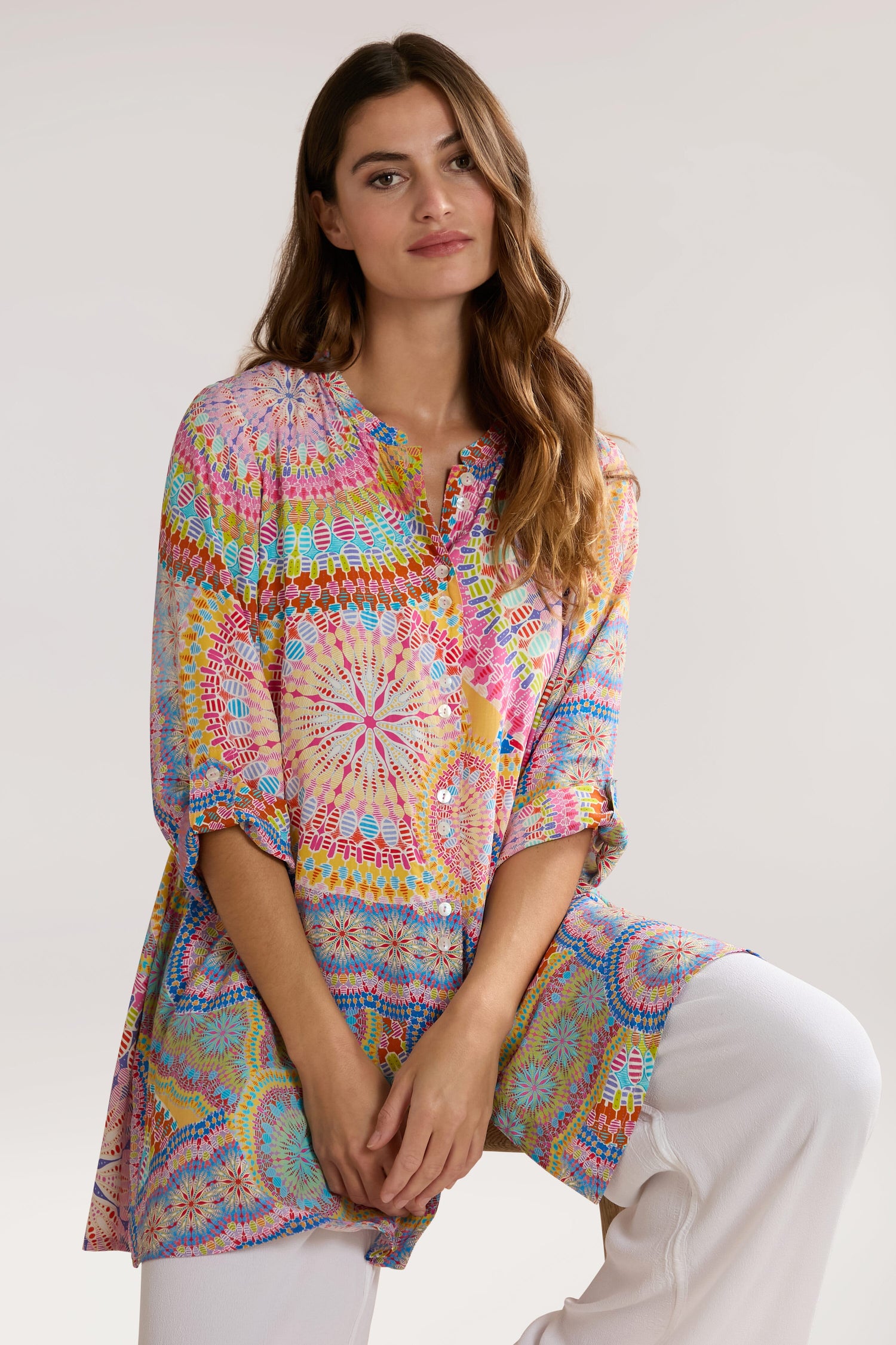 A woman with long brown hair wearing a Circle Mandala Print Shirt made of pure viscose and white pants poses against a plain background.