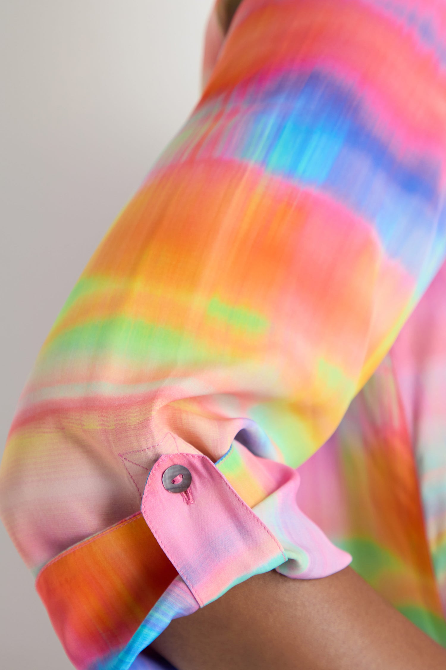 A close-up of a rolled sleeve on the Painted Horizon Flare Shirt, featuring a vibrant rainbow pattern and a visible pink button.