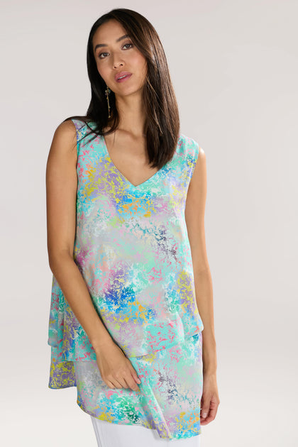 A woman with long dark hair is wearing a sleeveless, asymmetrical Marbled Cloud Print Frill Top made from pure viscose. She stands against a plain light background.