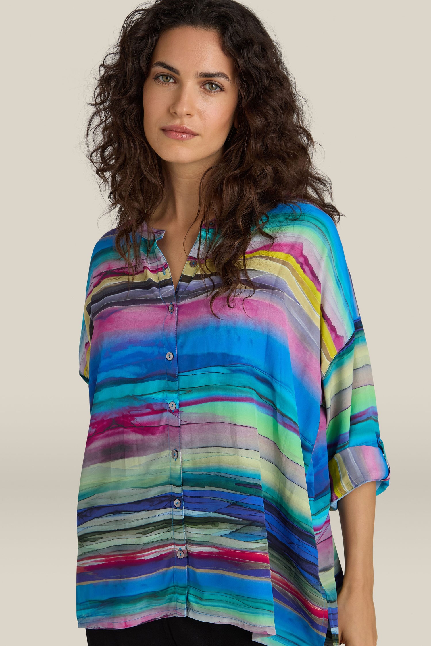 A woman wearing the Watercolour Landscape Boxy Shirt with a multicolored striped pattern and boxy fit, standing against a neutral background with her long, wavy hair cascading down.