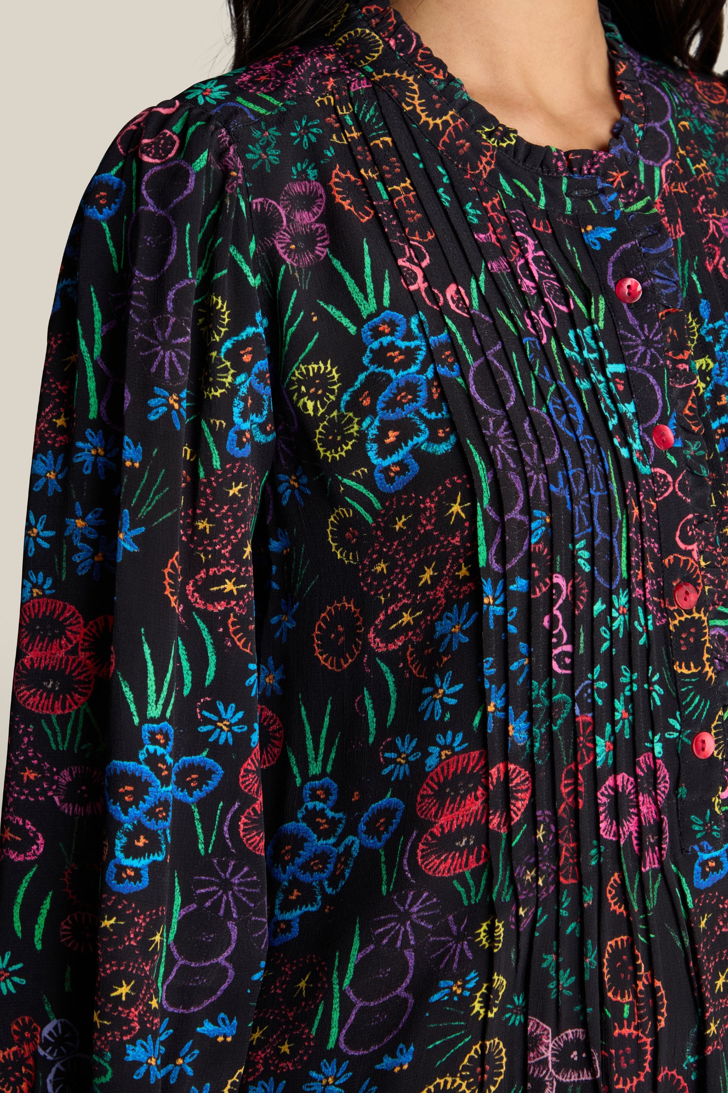 Close-up of a person wearing the Floral Embroidery Print Tunic, a black shirt adorned with colorful floral embroidery, vertical pleats, and buttons near the grandad collar.