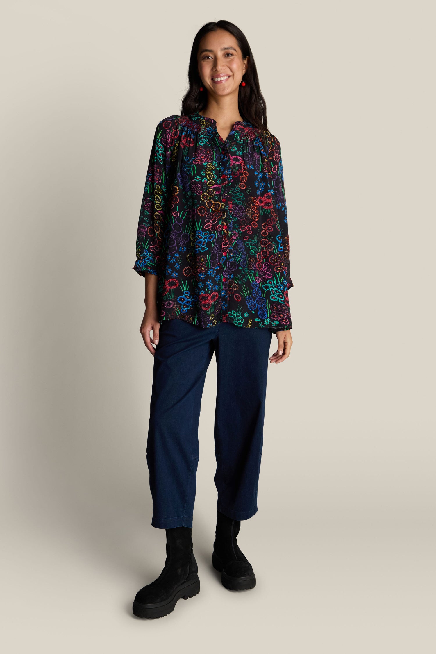 Person wearing an Embroidered Floral Print Shirt with 3/4 length sleeves, dark blue pants, and black boots, standing against a plain background.