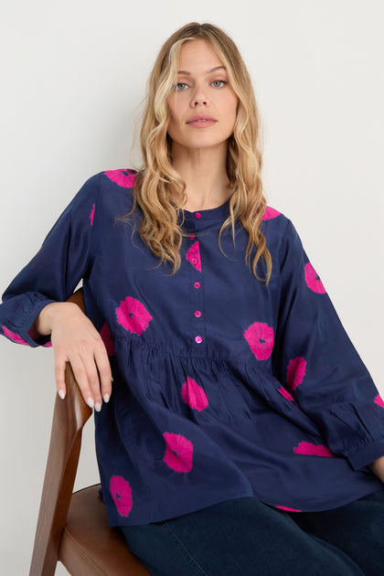 Woman with long blonde hair wearing the Shibori Spot Silk Shirt, seated on a wooden chair against a plain light background.