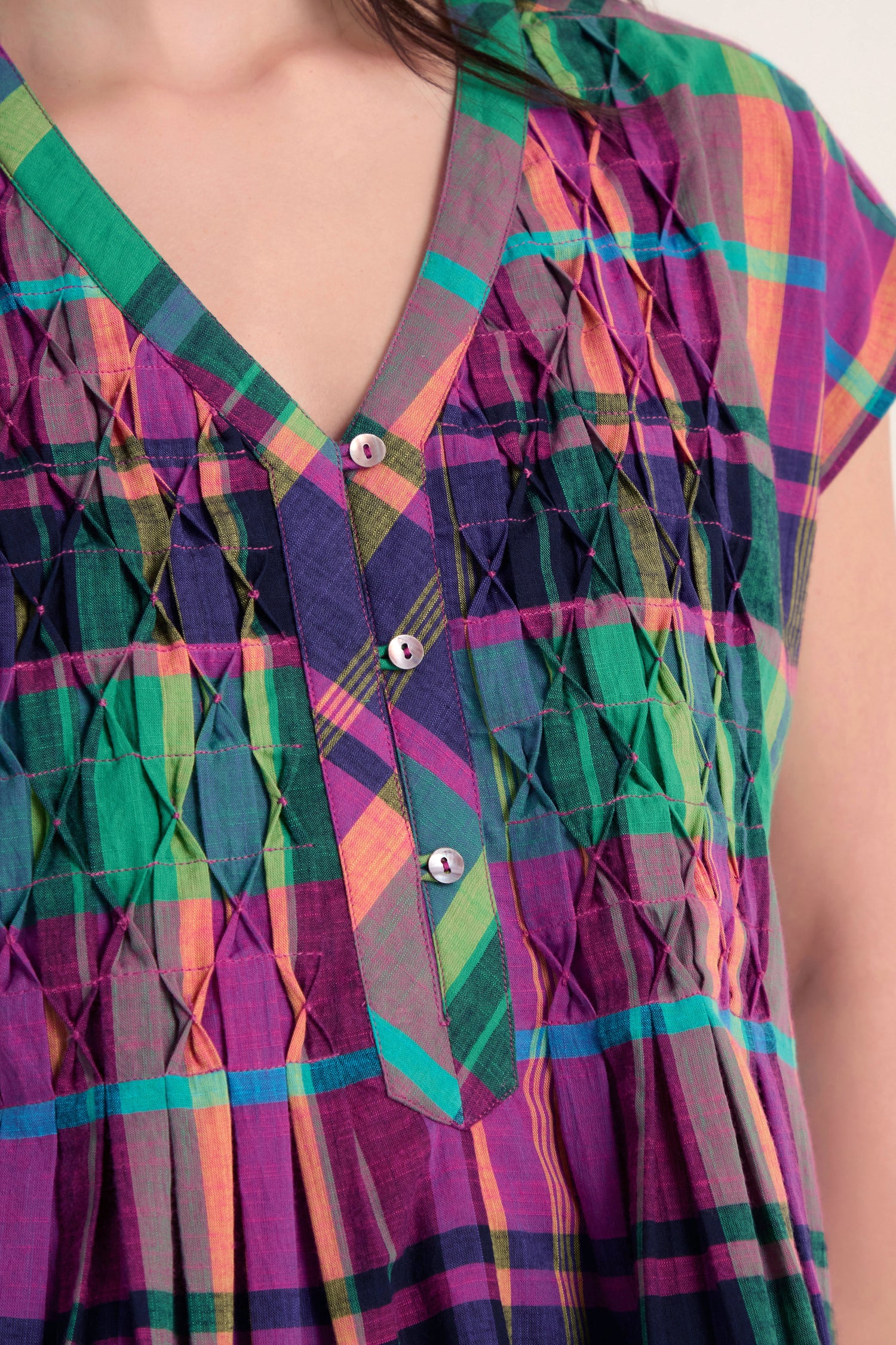 Close-up of a person wearing the Madras Check Pleated Top, featuring colorful checks, button details, decorative stitching near the collar, and a soft pure cotton finish.