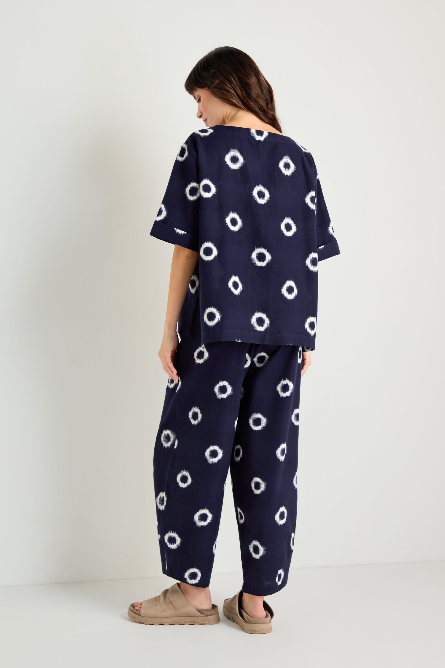 A person stands facing away, wearing an Ikat Circles Cotton Top with an oversized boxy silhouette and tan sandals, set against a plain white background.