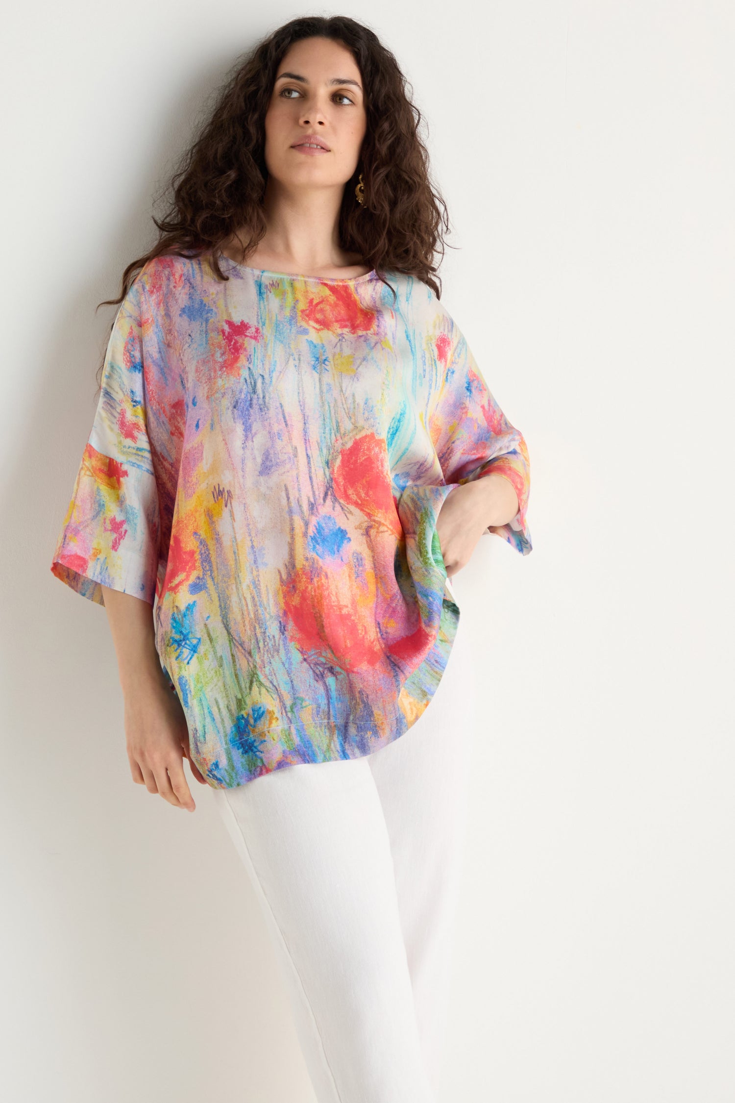 A person wears the Meadow Dreams Boxy Tunic, an artistic floral top with a relaxed fit, paired with white pants against a plain white background.