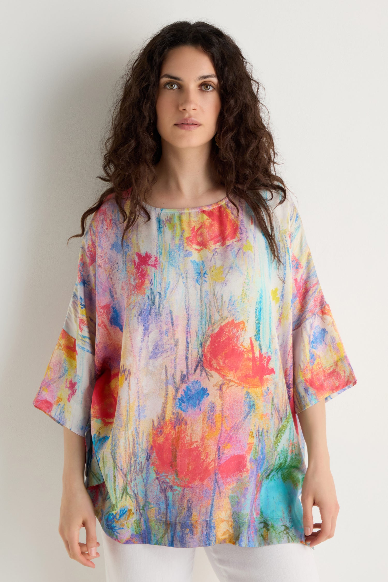 A woman with long curly hair wears the Meadow Dreams Boxy Tunic and white pants, standing against a plain white background.