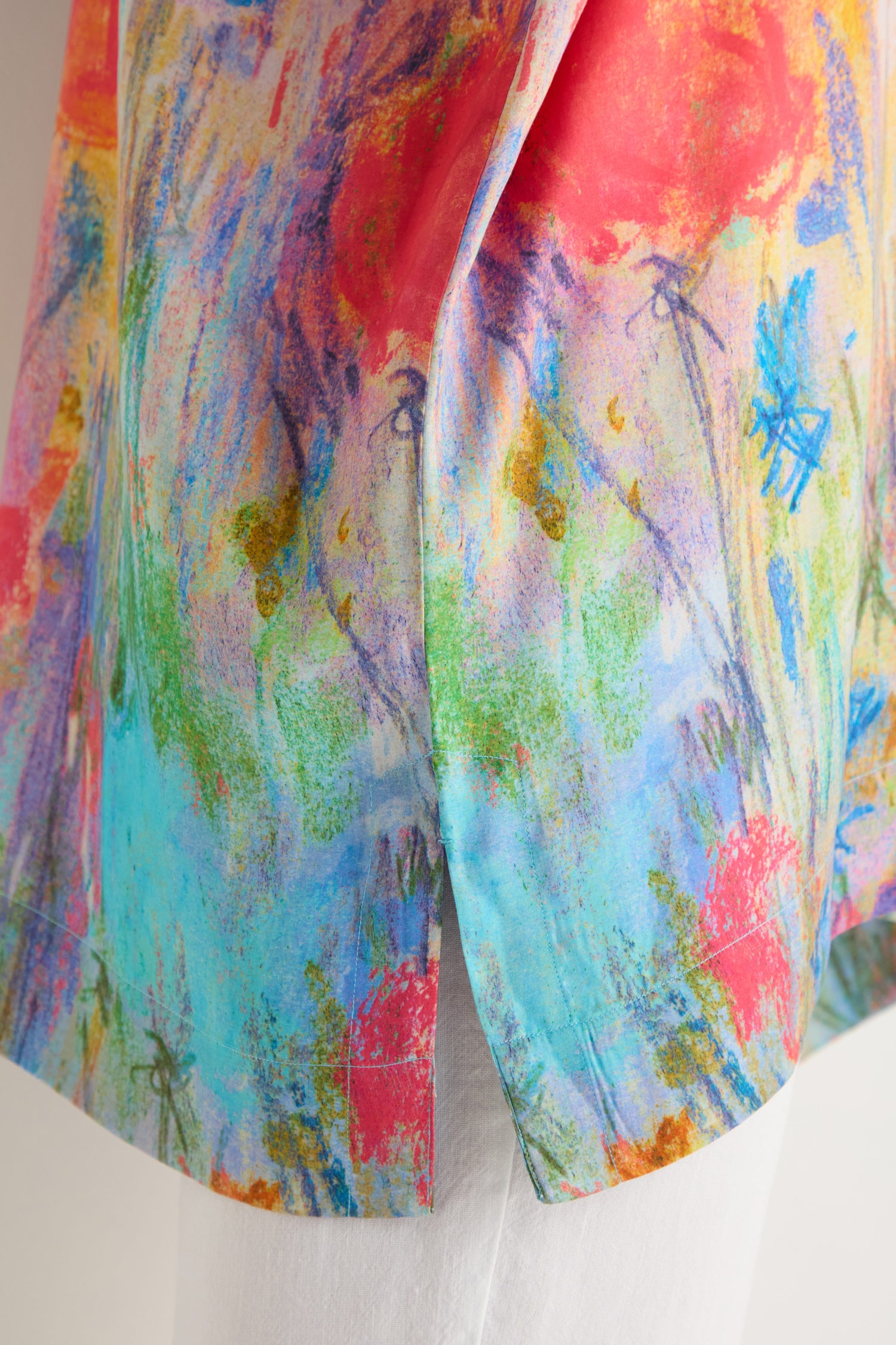 A close-up of the Meadow Dreams Boxy Tunic, featuring a colorful abstract pattern, relaxed fit, and side hem slit, styled over white pants.