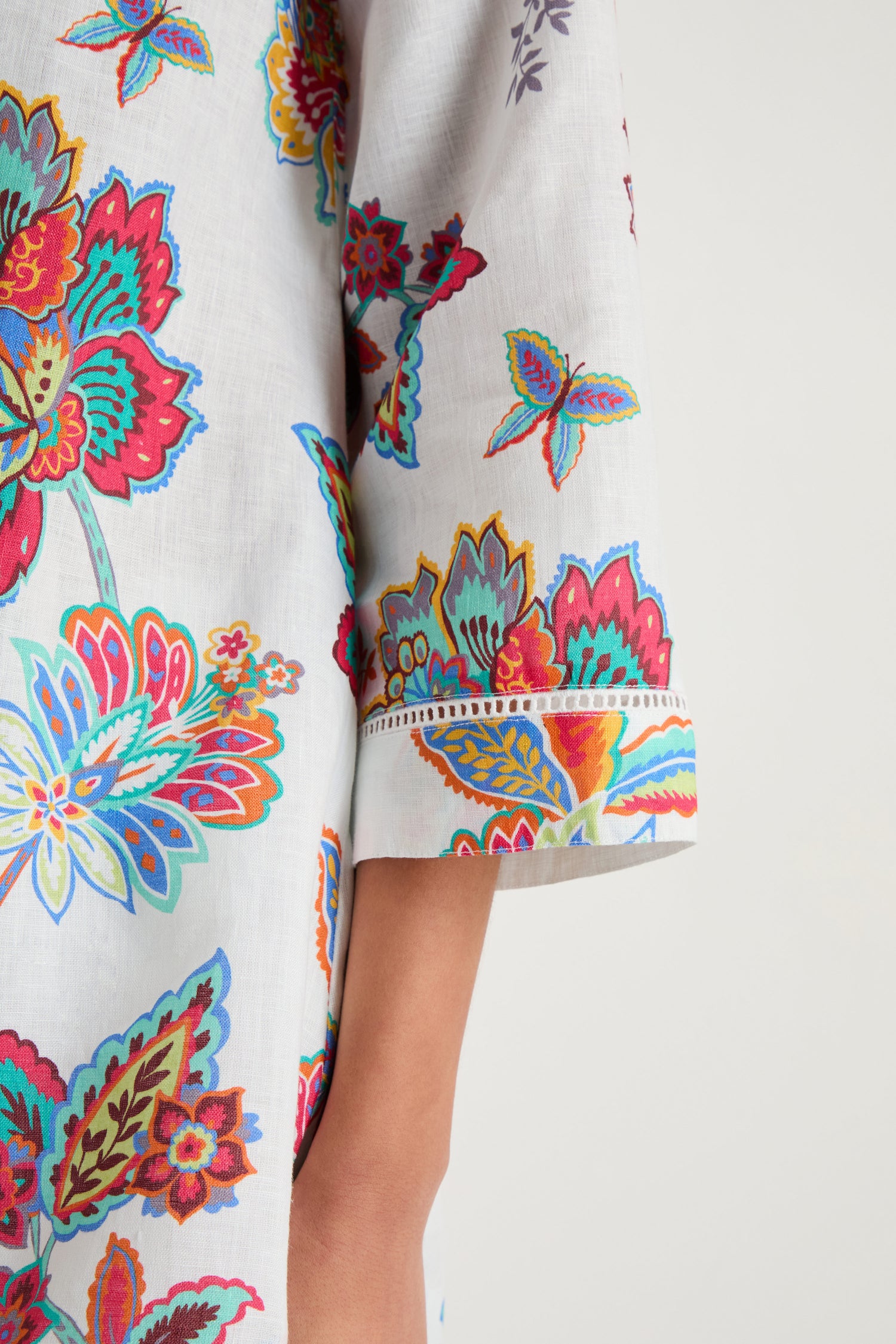 A close-up of a person wearing the Botanical Linen Flare Shirt, featuring colorful botanical prints on white linen, with the sleeve and part of the arm visible.