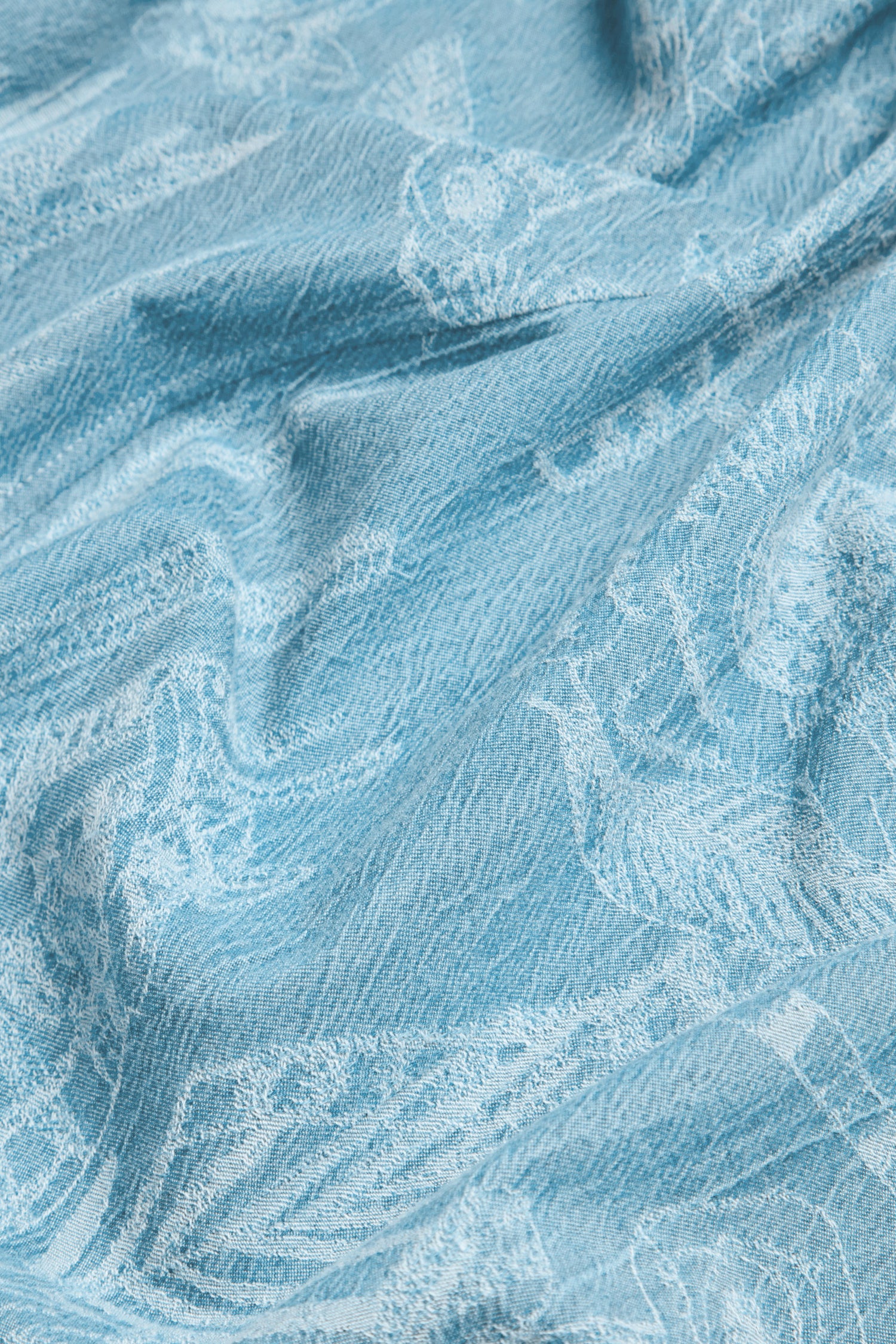 Close-up of the Floral Jacquard Cotton Shirt in light blue, showing its subtle woven animal and floral patterns with a slightly wrinkled texture.