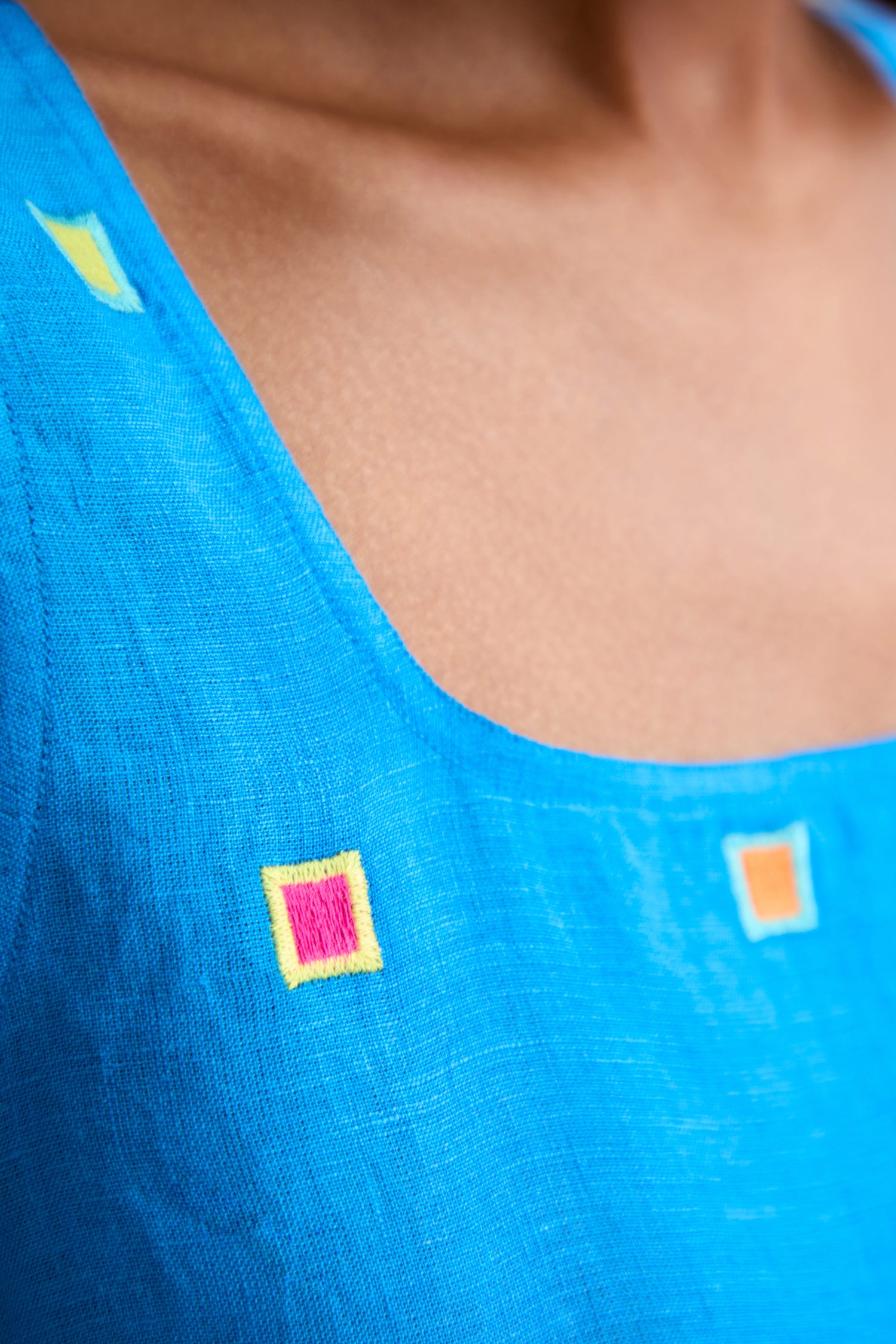 Close-up of a person wearing the Embroidered Squares Linen Vest in blue, featuring hand-finished yellow, orange, and pink square embroidery near the neckline and a relaxed fit.