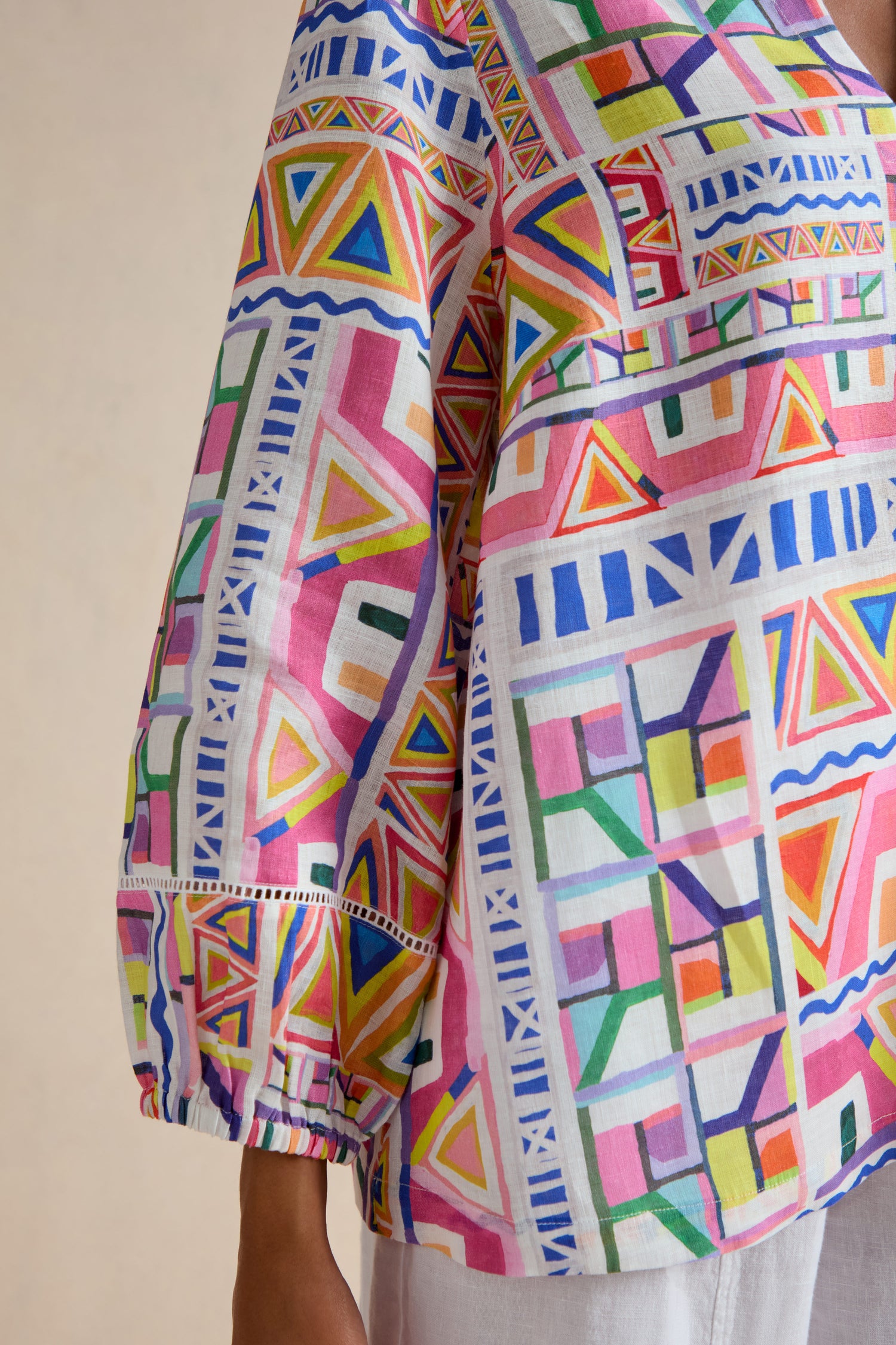 A person wears the Painted Geo Linen Top, featuring a colorful geometric pattern in pink, blue, yellow, green, and white. Only the torso and part of one balloon sleeve are visible.
