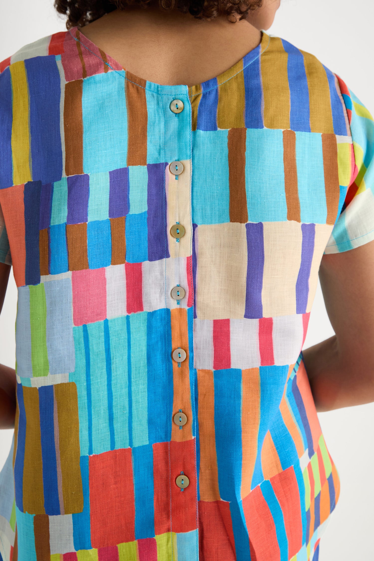 A person shown from behind wearing the Painted Stripes Linen Top—a relaxed fit shirt with geometric stripes and buttons down the back.