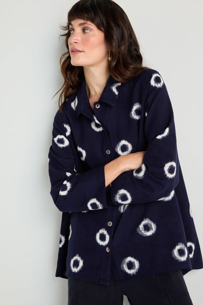A woman stands against a light wall with arms crossed, wearing the Ikat Circles Cotton Shirt in navy with a white circular pattern.