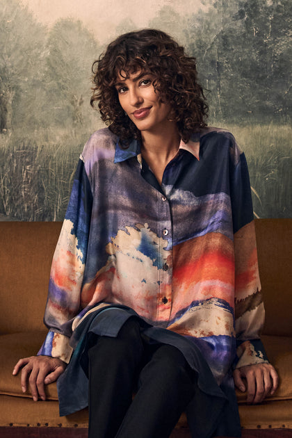 A person wearing a Moontide Silk Shirt, a tunic-length, long-sleeved garment featuring a multi-colored abstract landscape print.
