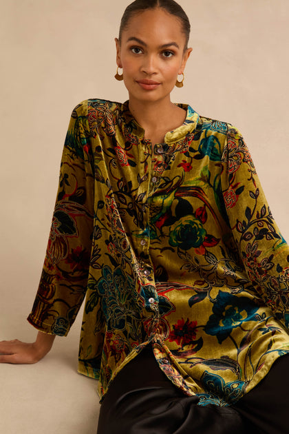 A person wearing a Silk Velvet Floral Devore Shirt, a long-sleeved, button-down top featuring a multi-colored floral pattern on olive-green fabric.
