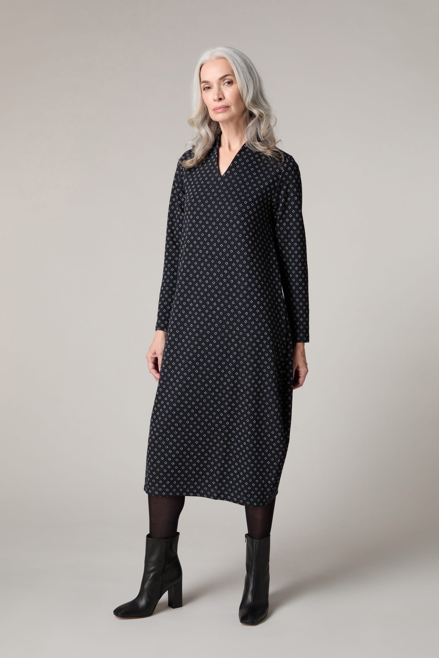 A woman wearing a Lurex Spot Jersey Dress, a black polka dot dress with a V-neck.