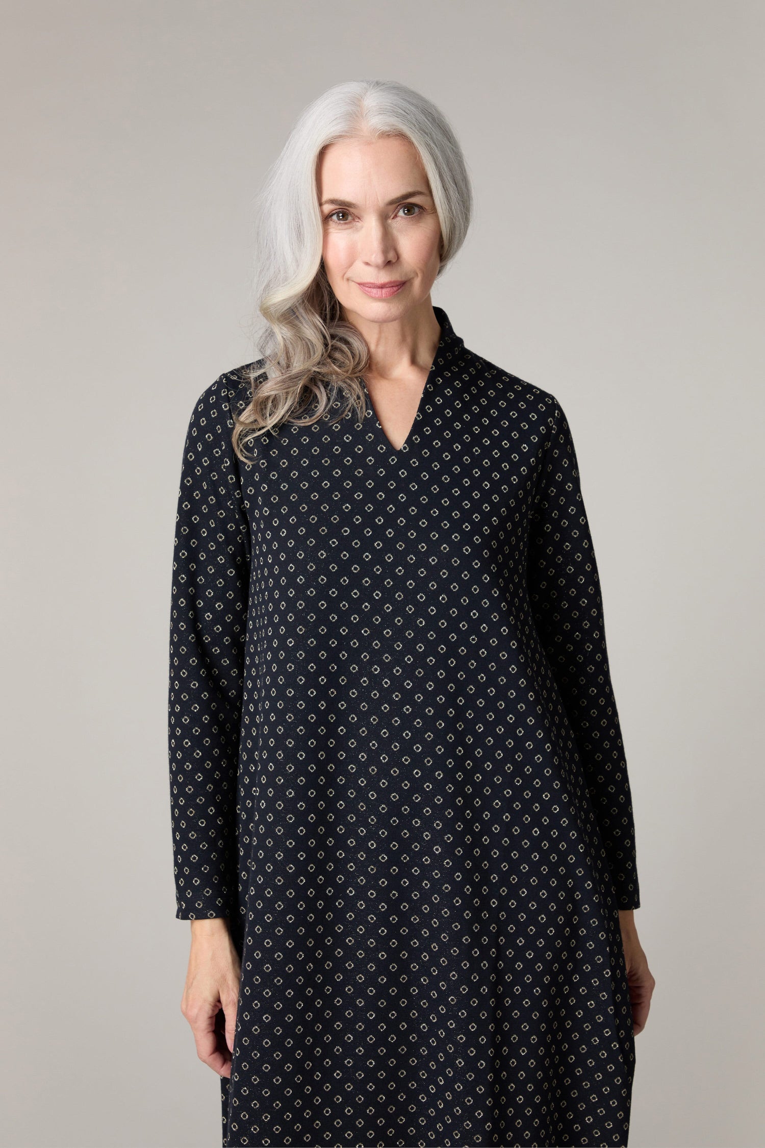 A woman wearing a Lurex Spot Jersey Dress, featuring a spotted pattern and signature bubble shape.