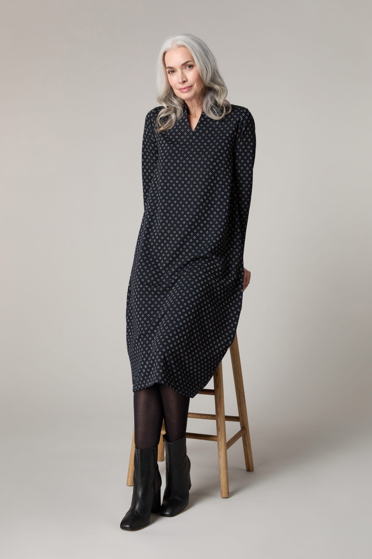 A woman sitting on a stool wearing a black polka dot Lurex Spot Jersey Dress.