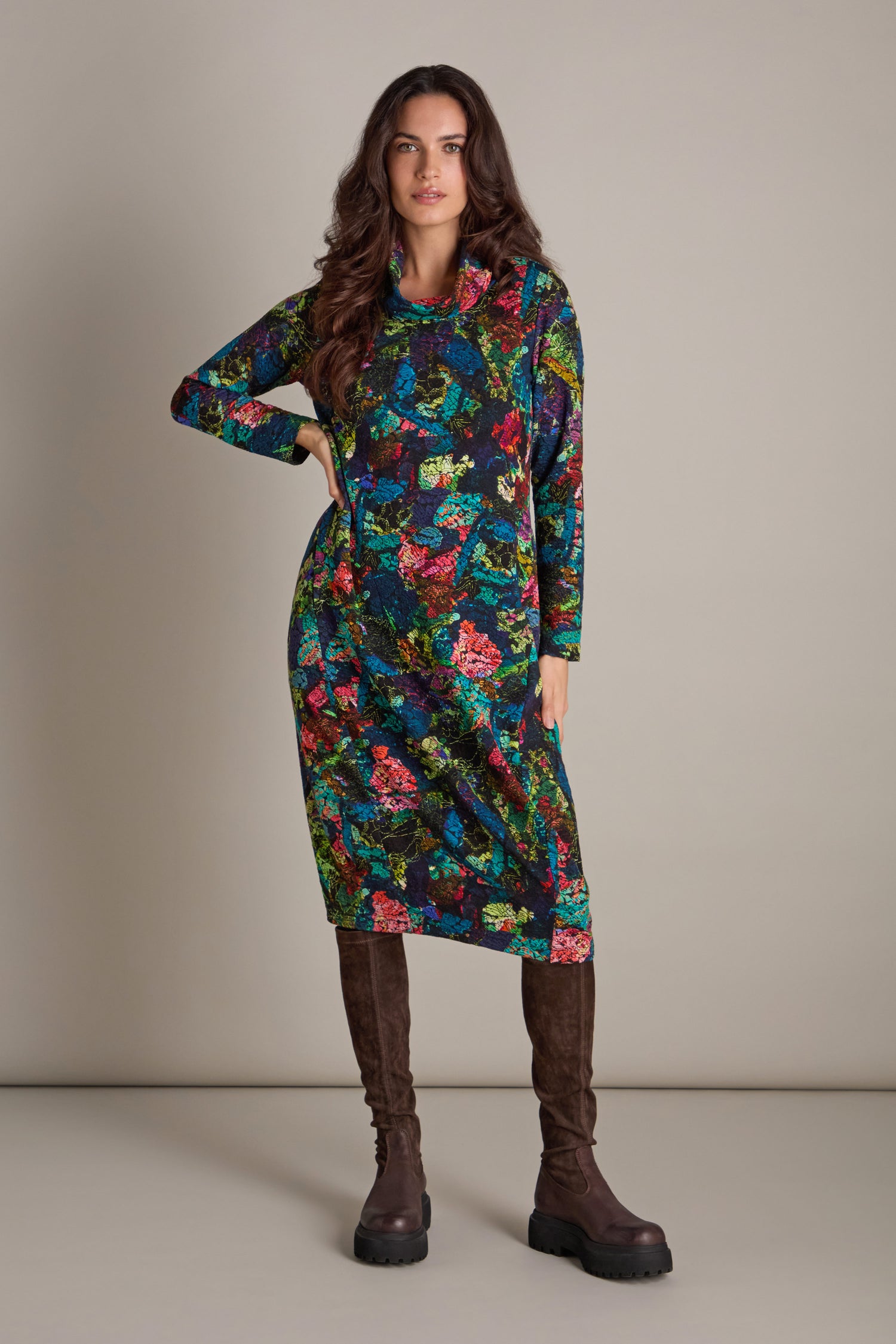 A woman stands wearing an Abstract Floral Jersey Bubble Dress, complemented by brown knee-high boots against a plain background.